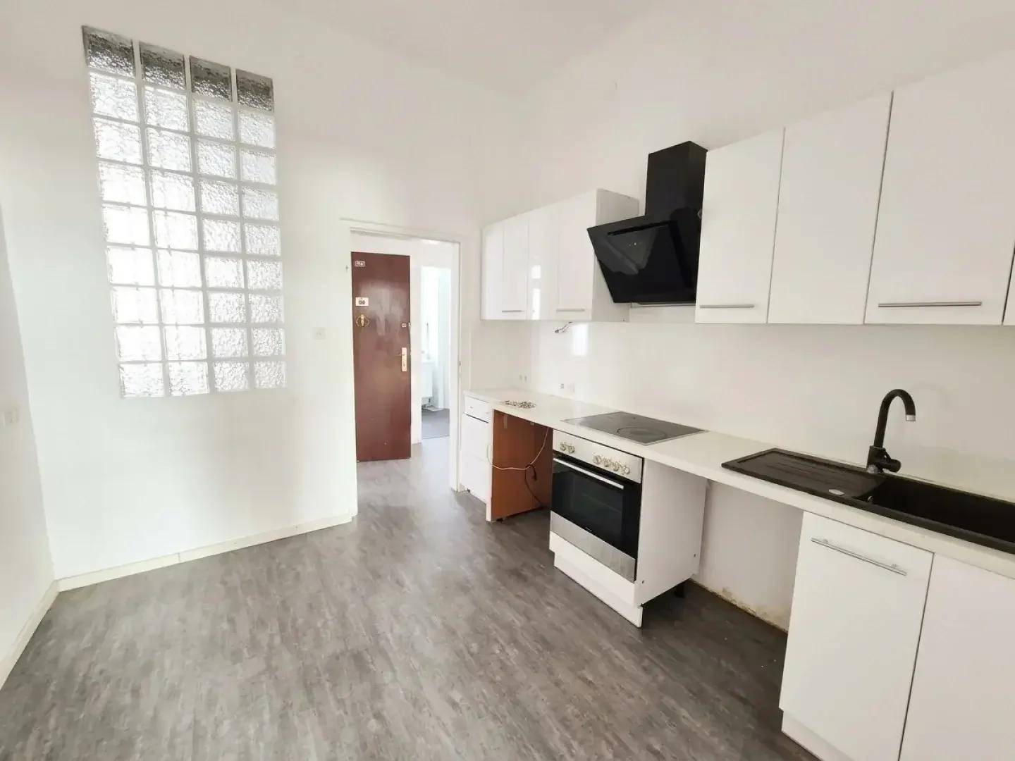 Moderne Küche mit weißen Schränken, schwarzer Spüle und Kochfeld, sowie einer Glasbausteinwand.