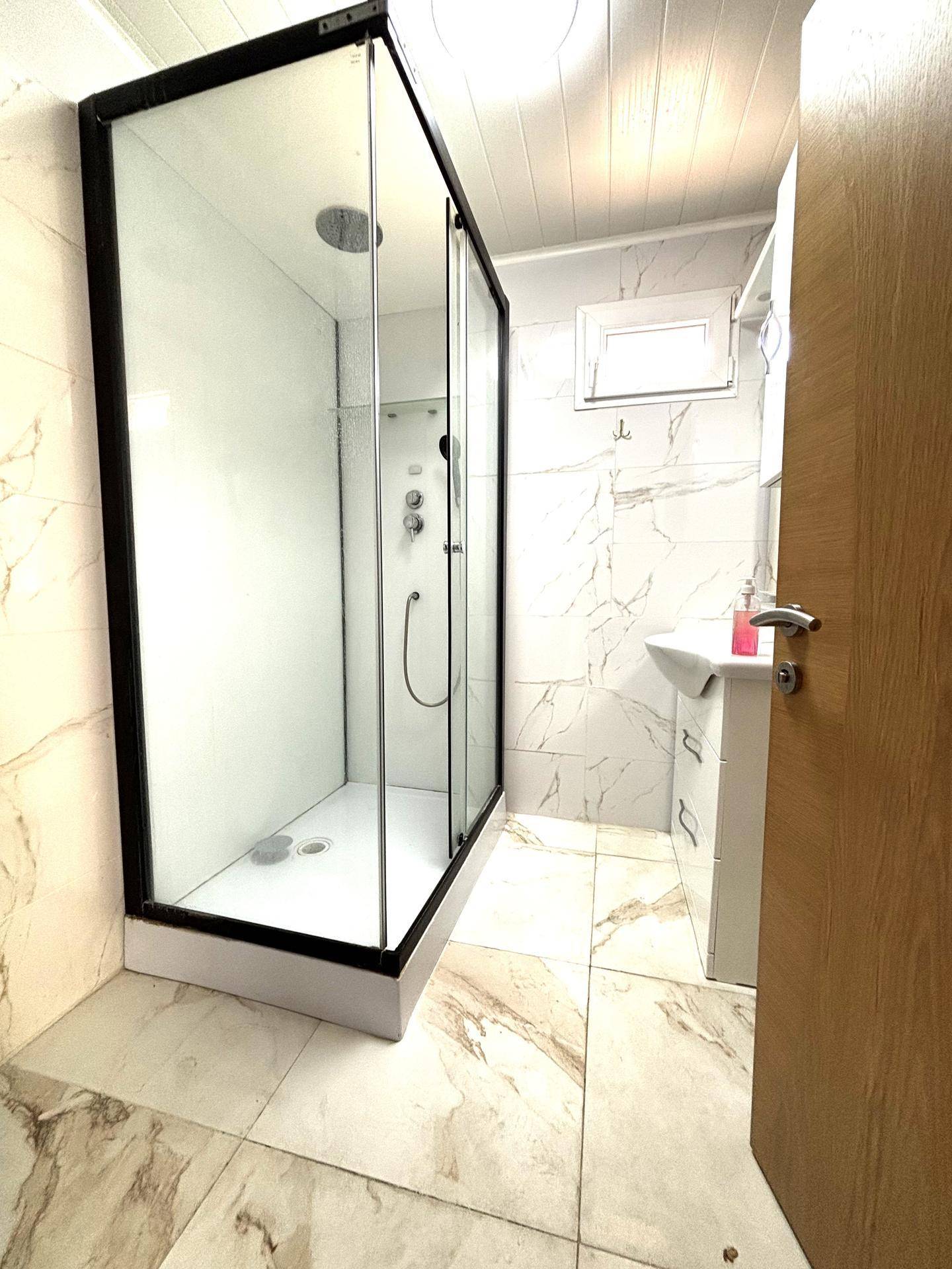 Modernes Badezimmer mit großer Duschkabine, Fliesenboden und kleinem Fenster für natürliche Belüftung.