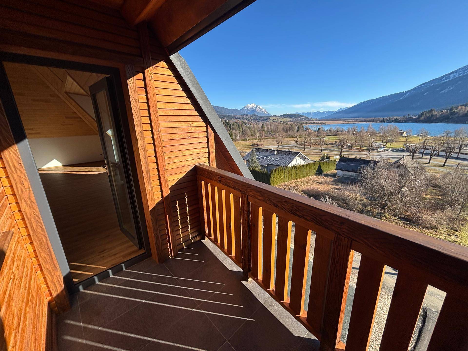 Geräumiger Balkon mit Holzboden und atemberaubendem Blick auf den See und die umliegenden Berge.