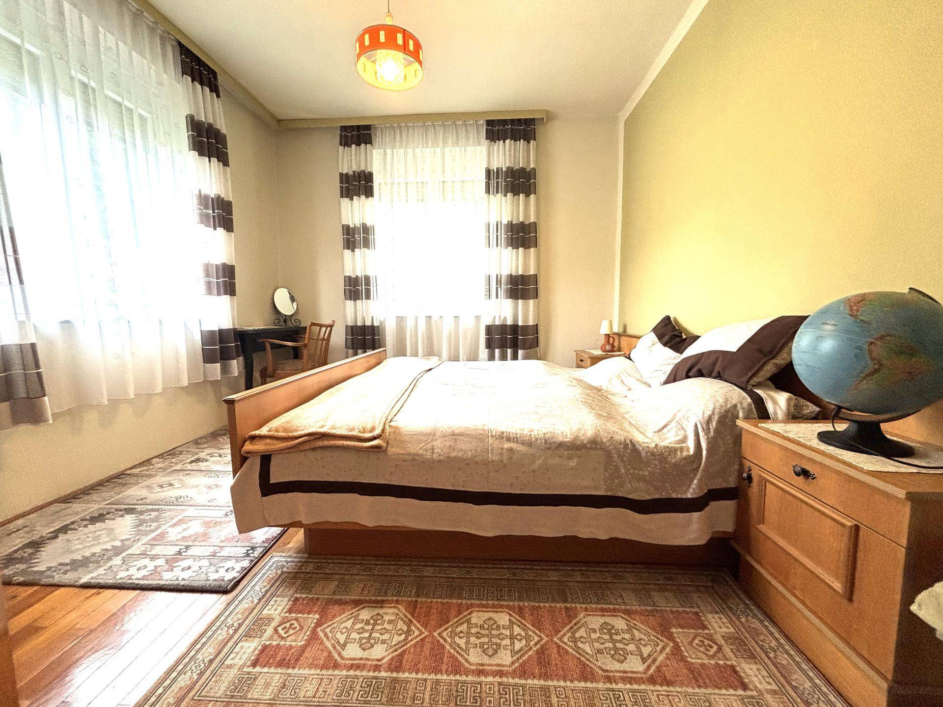Schlafzimmer mit Holzboden, großem Bett und Schreibtisch am Fenster.
