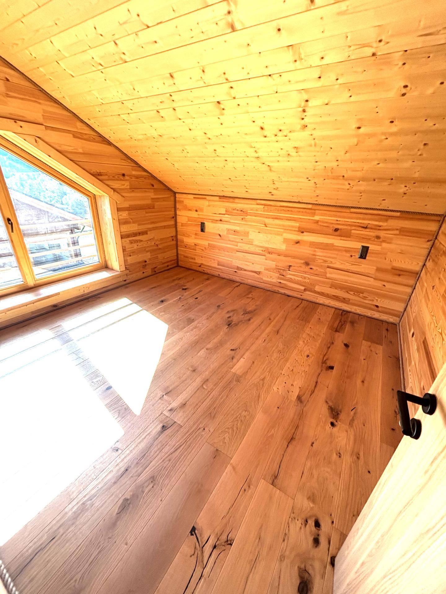 Gemütliches Zimmer mit Holzboden und -wänden, Dachschräge und sonnigem Ausblick.