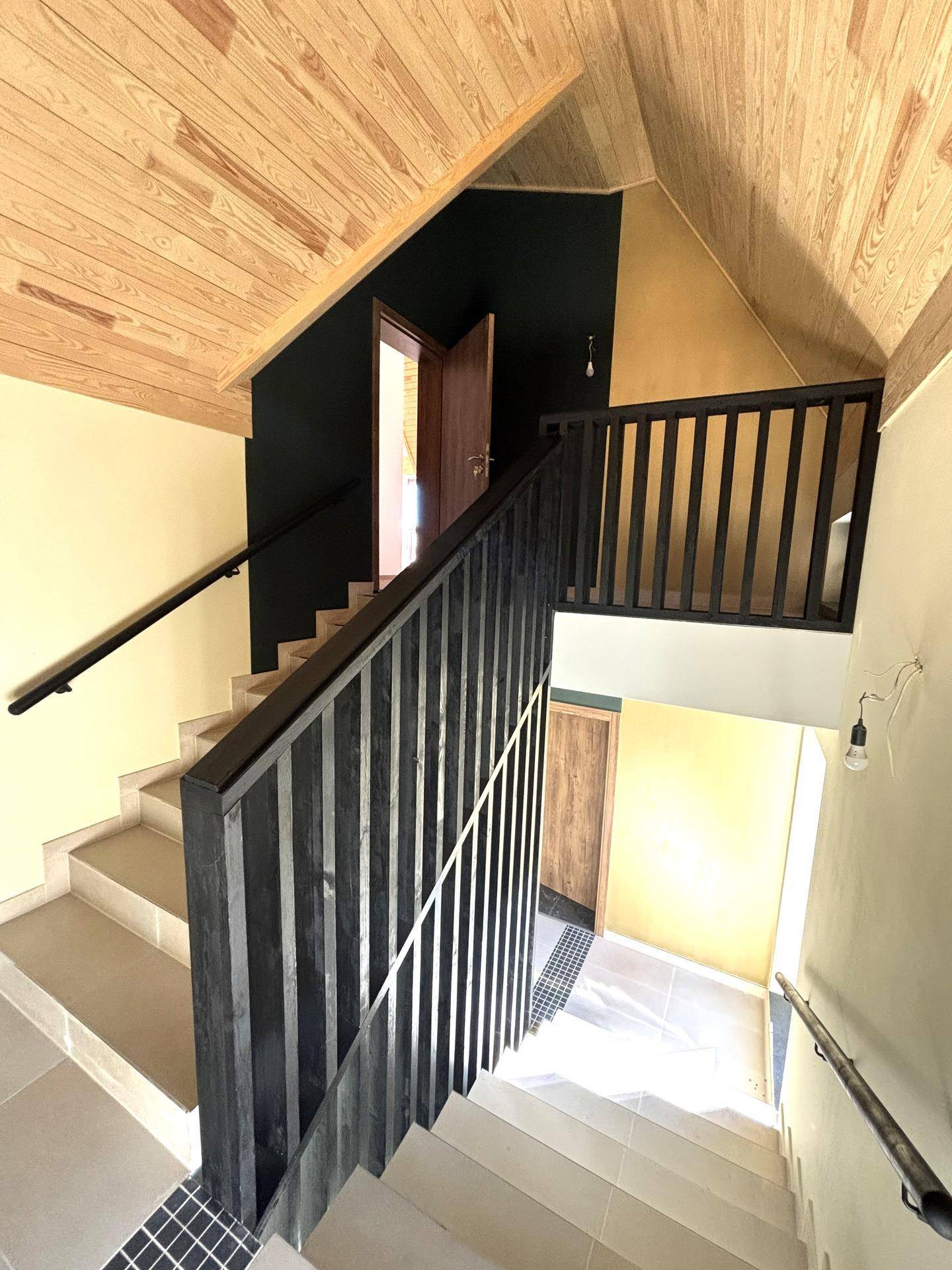 Treppenhaus mit Holzgeländer, Fliesenboden und Zugang zu den oberen Etagen.