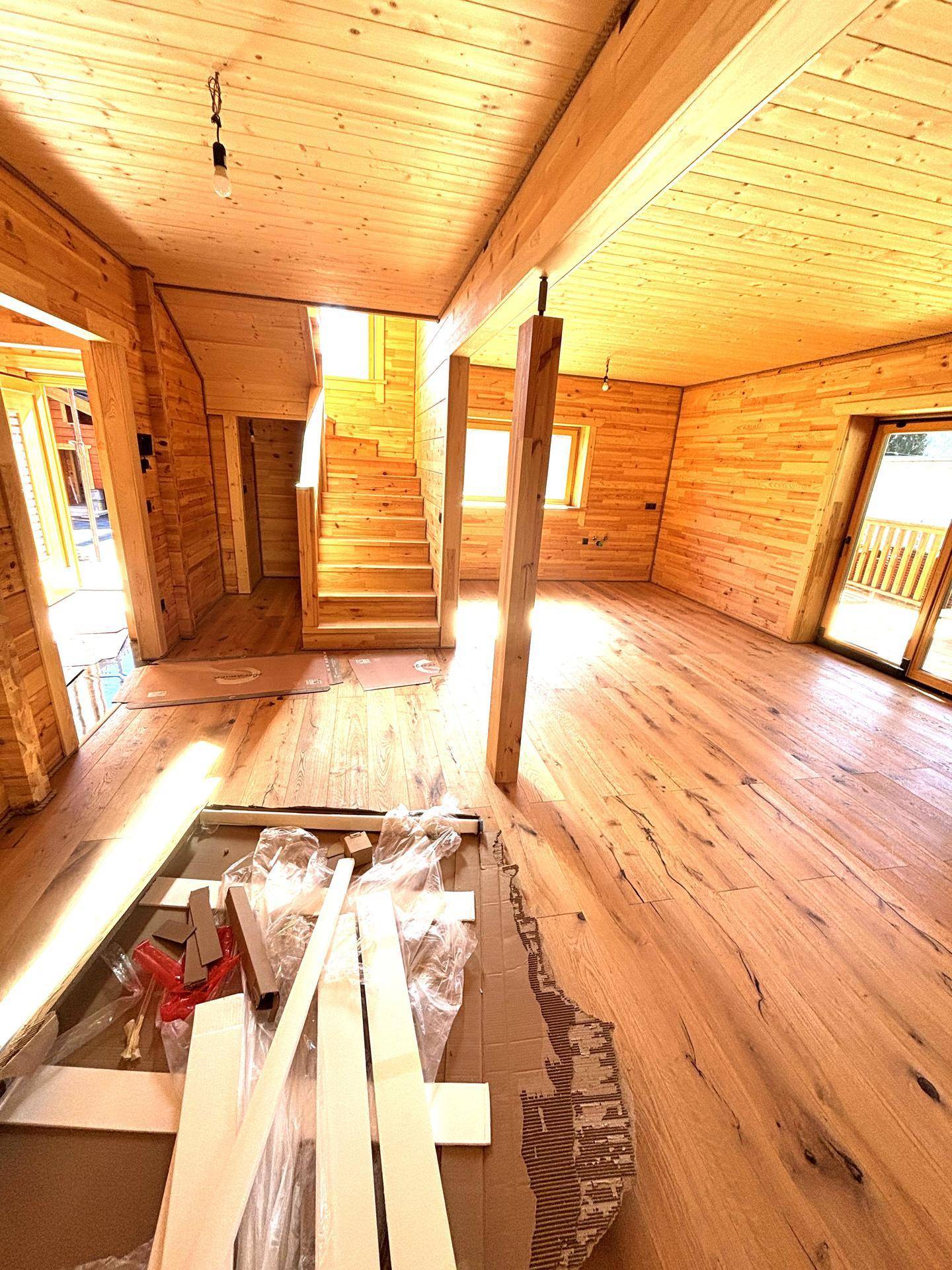 Großes Wohnzimmer mit Holzboden und Holzvertäfelung, viel natürliches Licht und Treppenaufgang.