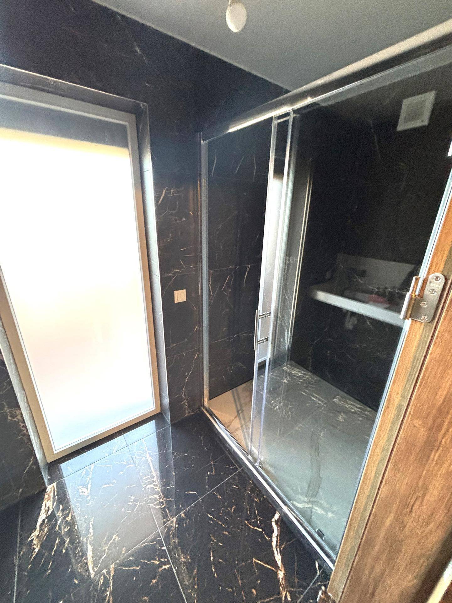 Moderne Duschkabine mit Glaswänden, dunklen Boden- und Wandfliesen in Marmoroptik.