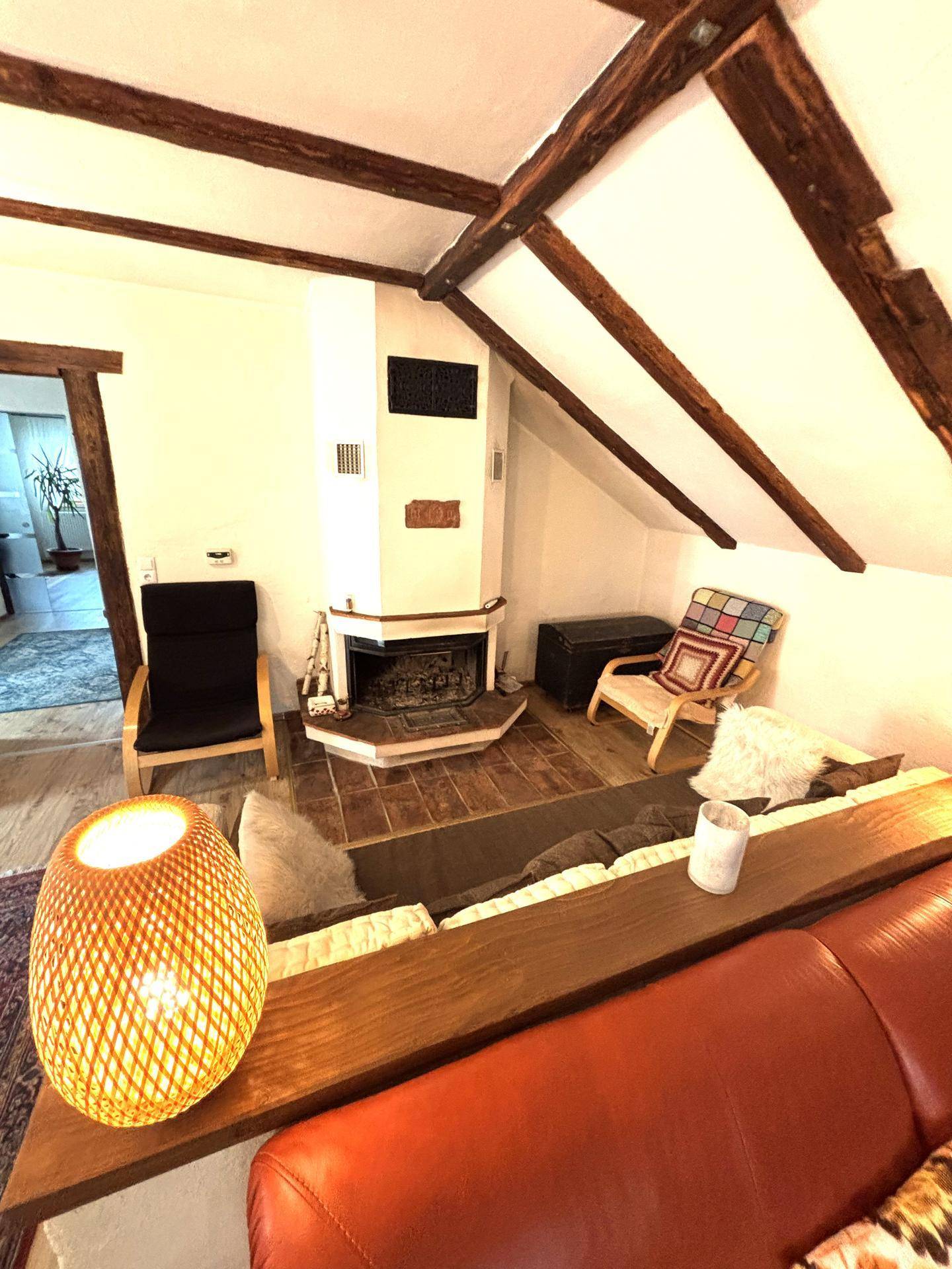 Gemütliches Wohnzimmer mit sichtbaren Holzbalken, Kamin und rustikalem Charme unter dem Dach.