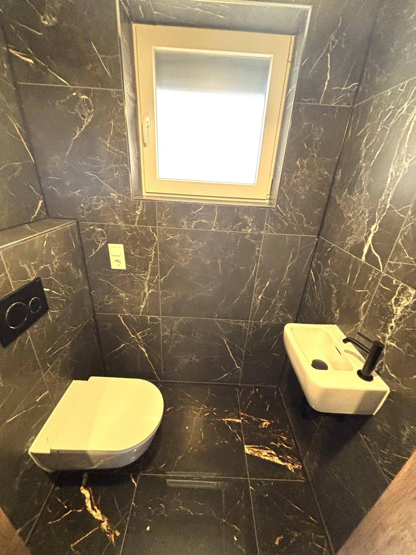 Modernes Gäste-WC mit dunklen Marmorfliesen, wandhängendem WC und kleinem Waschbecken.
