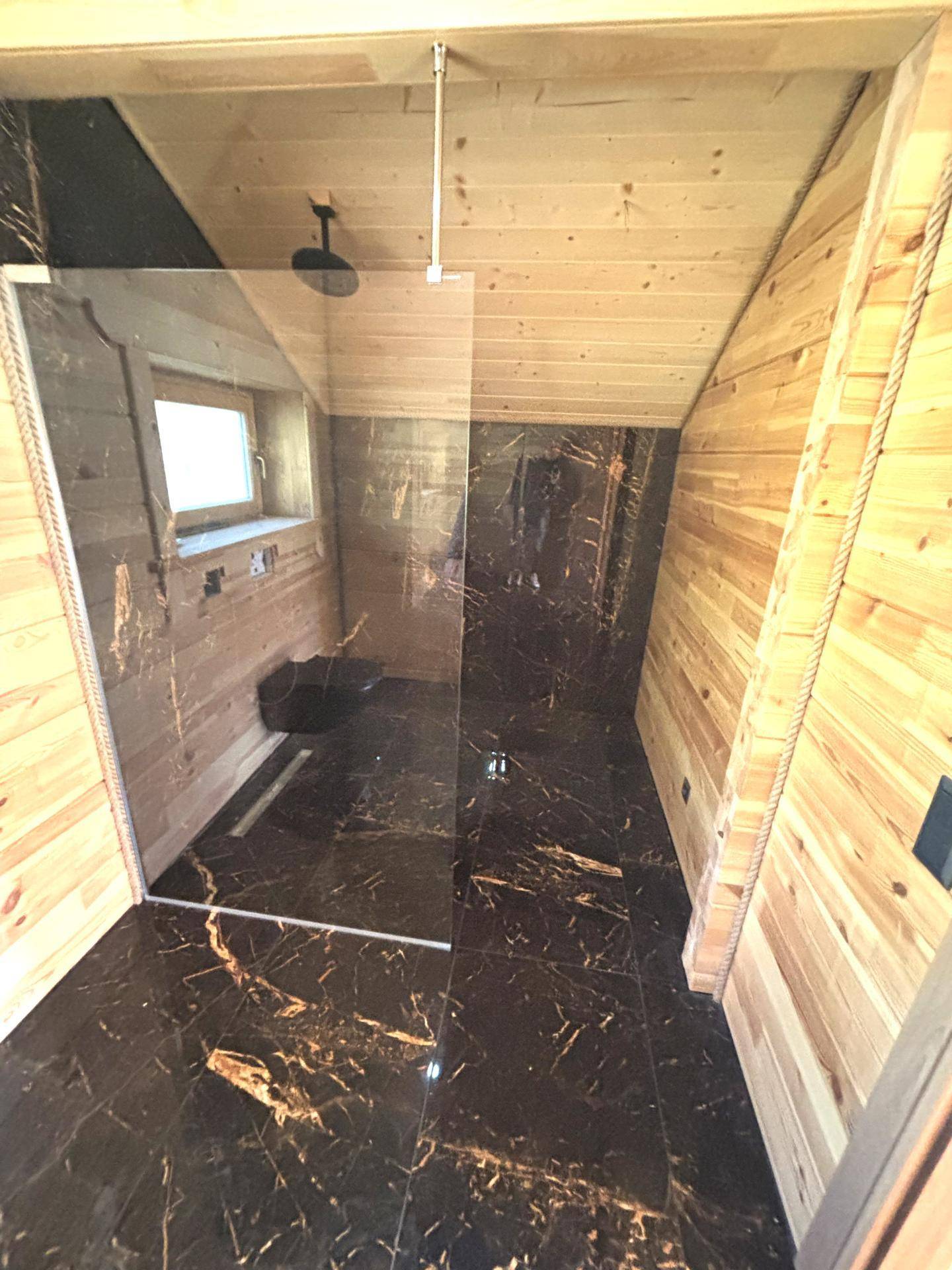 Geräumige begehbare Dusche in einem modernen Badezimmer mit dunklen Marmorfliesen und Holzvertäfelung.