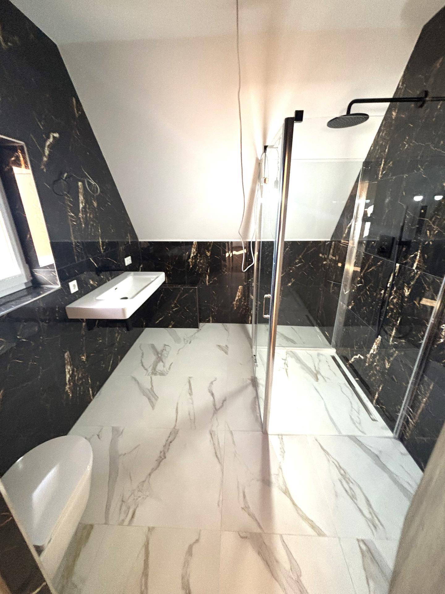 Modernes Badezimmer mit schwarzen Marmorfliesen, begehbarer Dusche und Dachschräge.