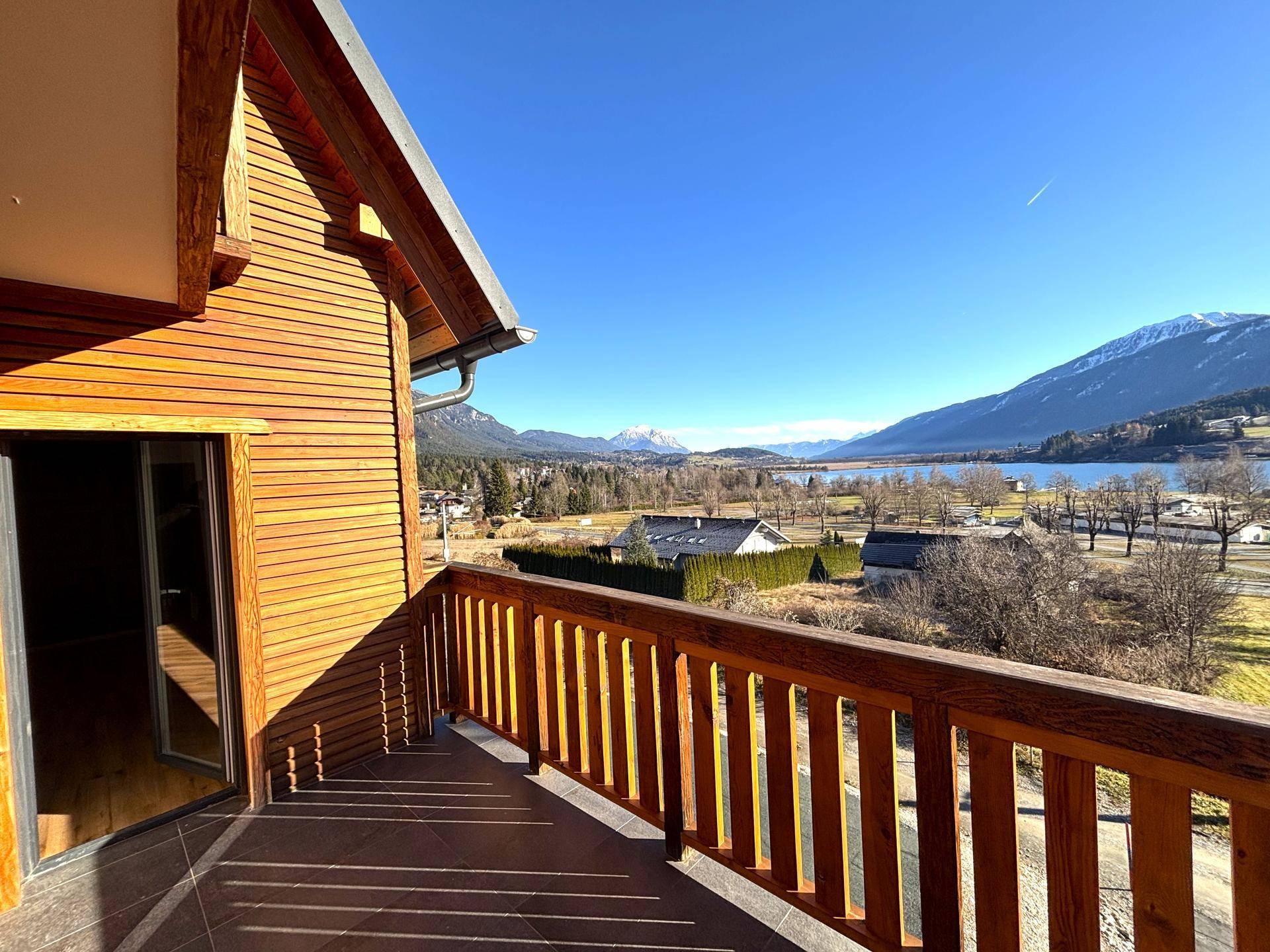 Geräumiger Holzbalkon mit Fliesenboden und weitem Blick auf den See und die Berge.