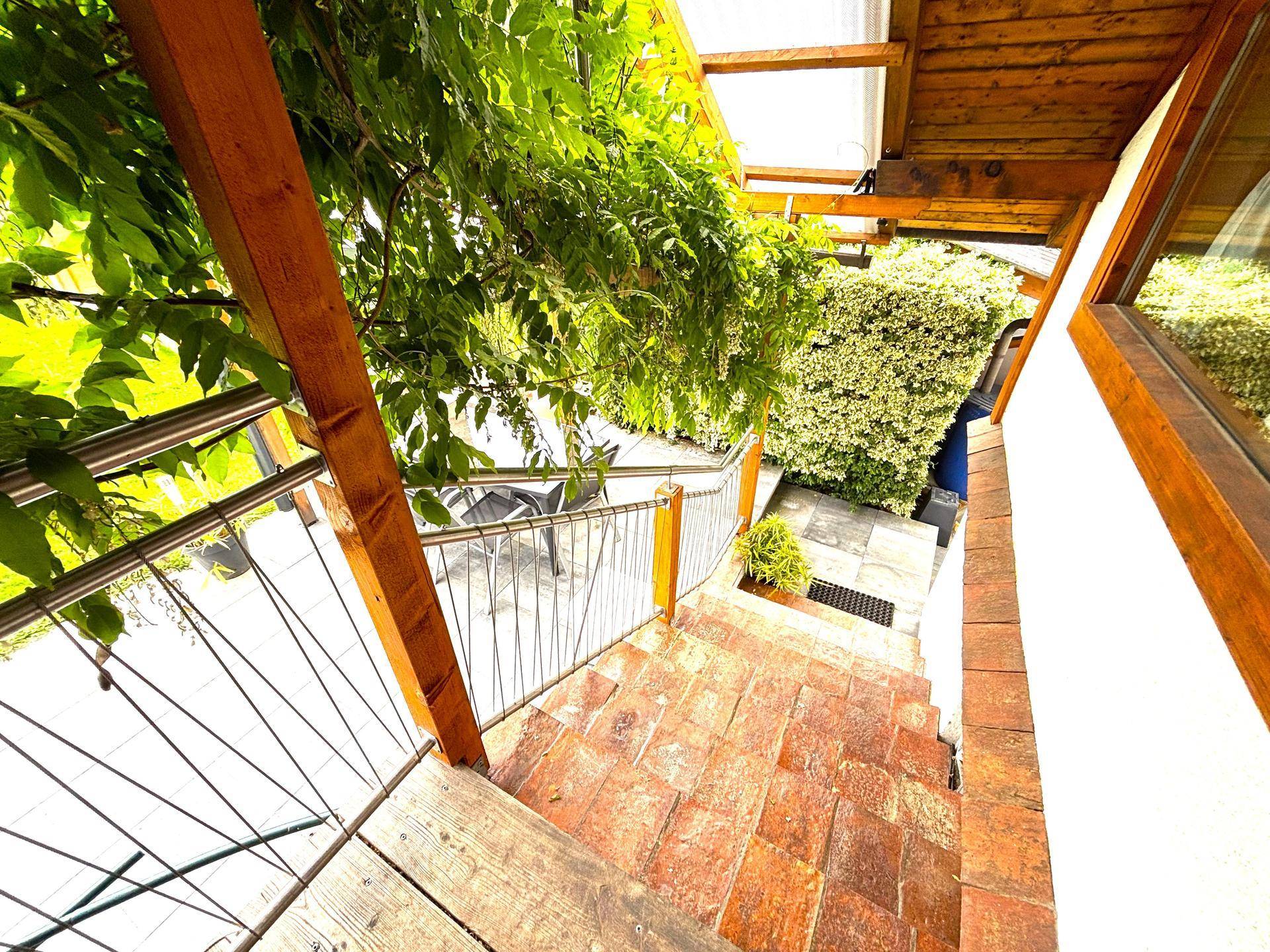Außentreppe führt zu einer gepflasterten Terrasse, umgeben von viel Grün.