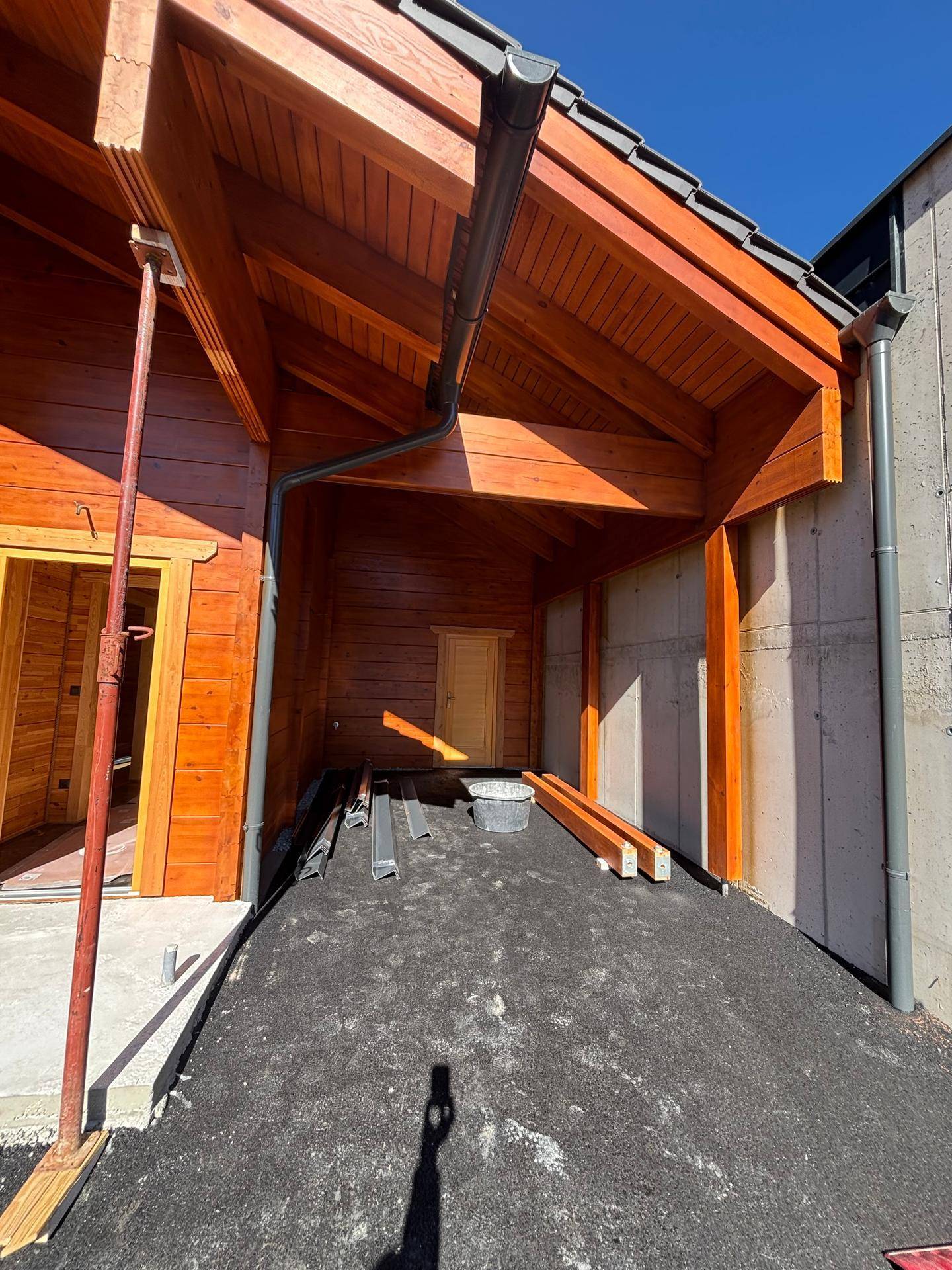 Überdachter Parkplatz oder Carport aus Holz neben dem Gebäude mit Betonwand.