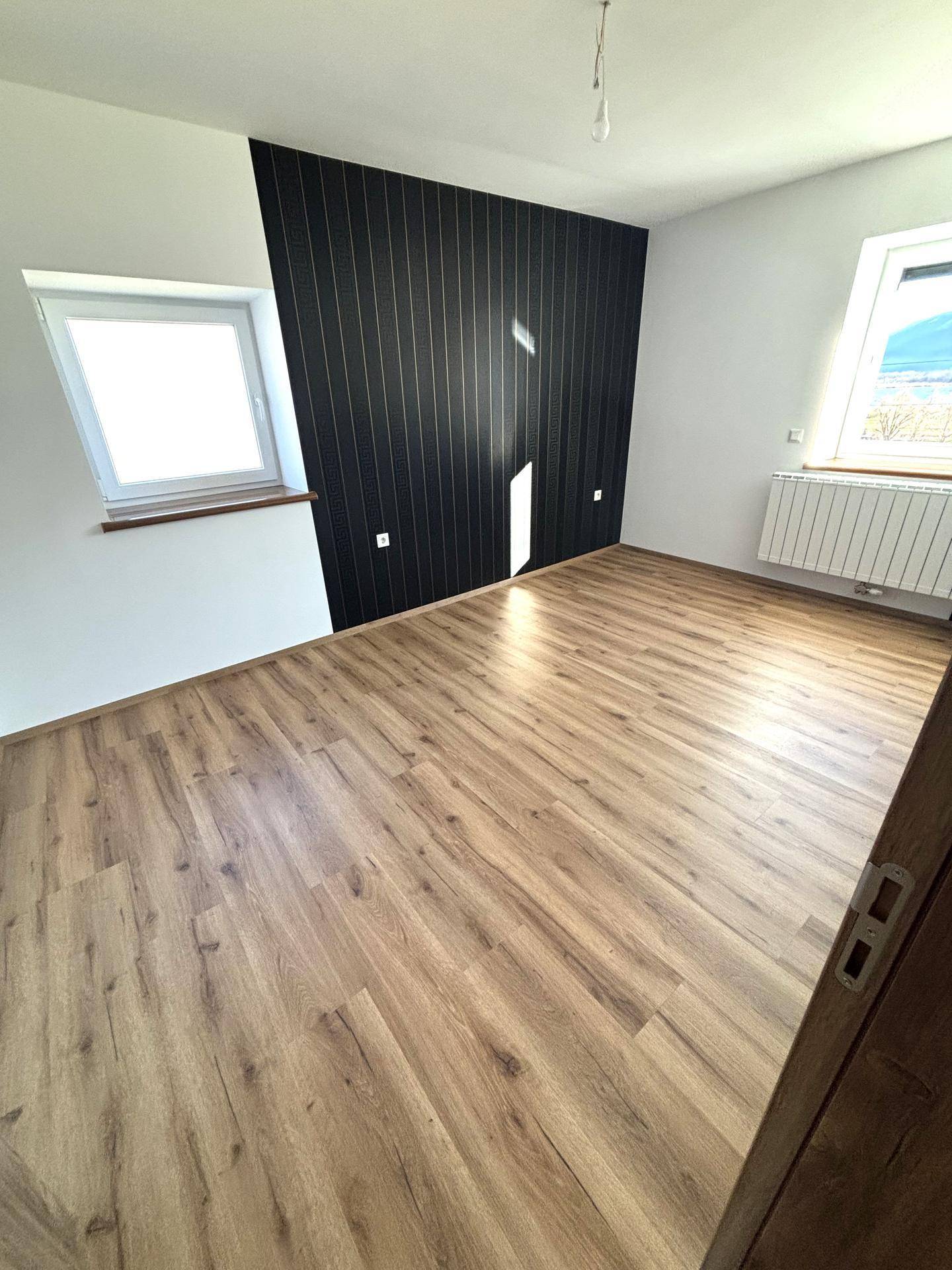 Schlafzimmer mit Laminatboden, einer schwarzen Akzentwand und zwei Fenstern für viel Licht.