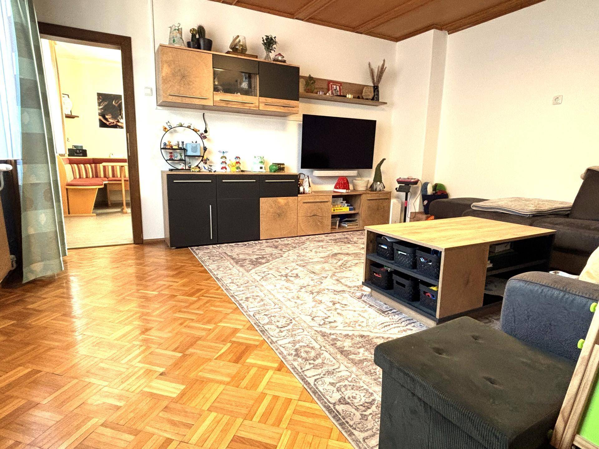 Gemütliches Wohnzimmer mit Parkettboden, Holzdecke und einem Teppich, der den Raum akzentuiert.