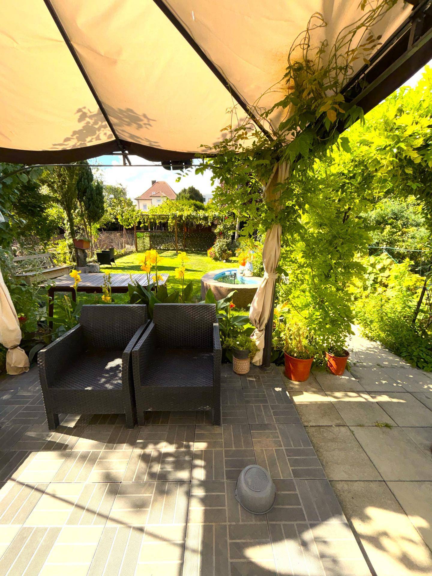 Gemütliche Terrasse mit Sitzgelegenheiten und Sonnenschutz, umgeben von üppigem Grün.