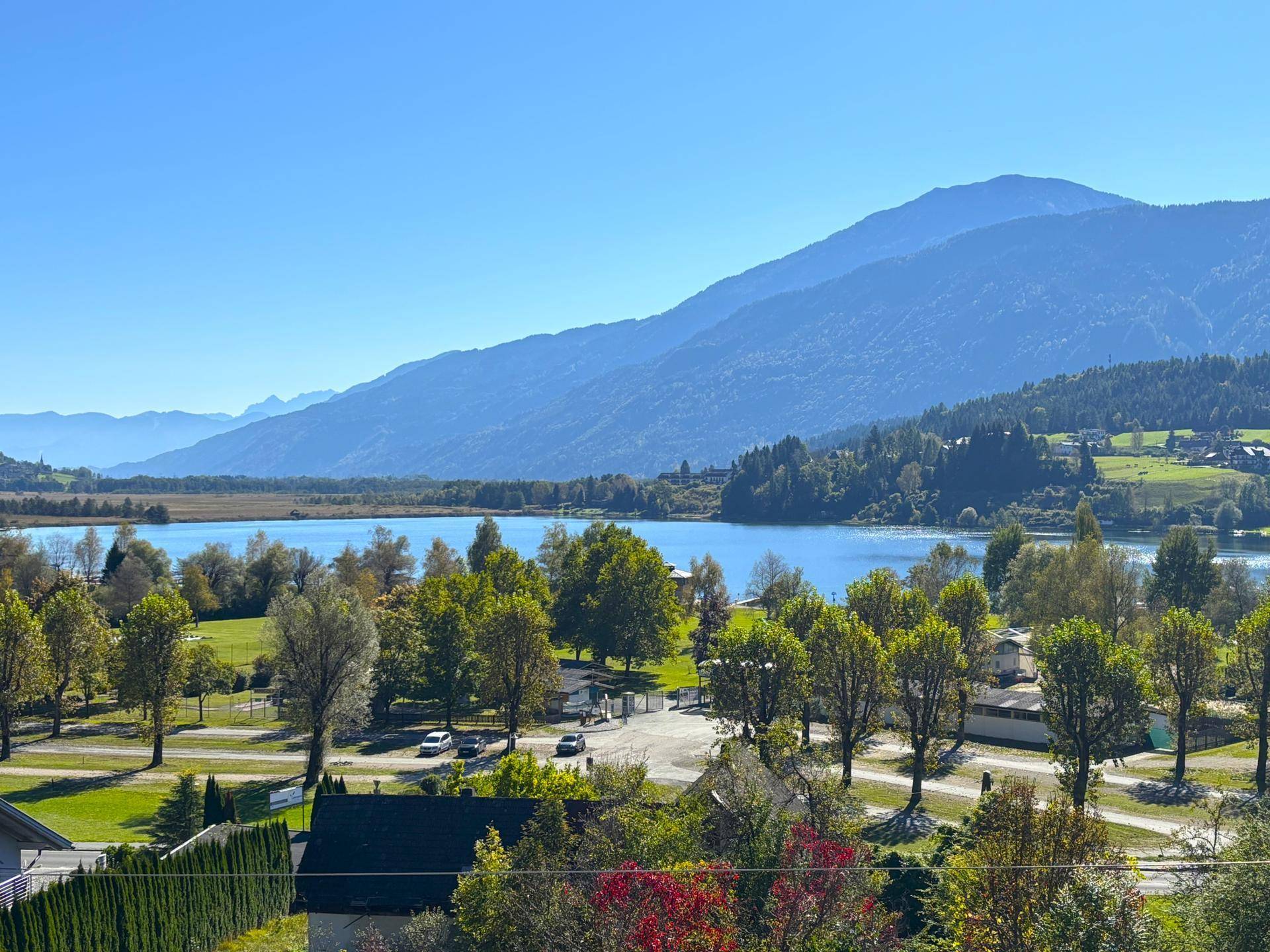 Malerischer Blick auf einen See und die umliegende Berglandschaft unter strahlend blauem Himmel.
