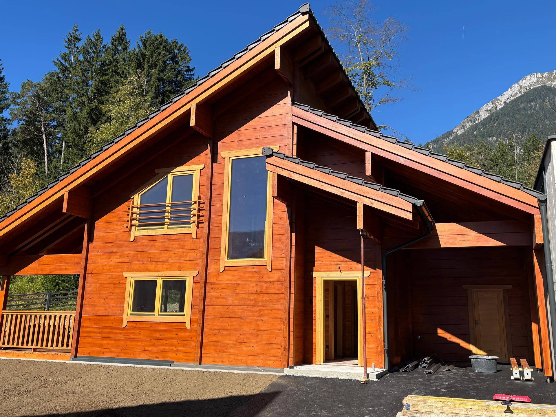 Vorderansicht eines neuen Holzhauses im Chalet-Stil mit großen Fenstern und Holzbalkon.