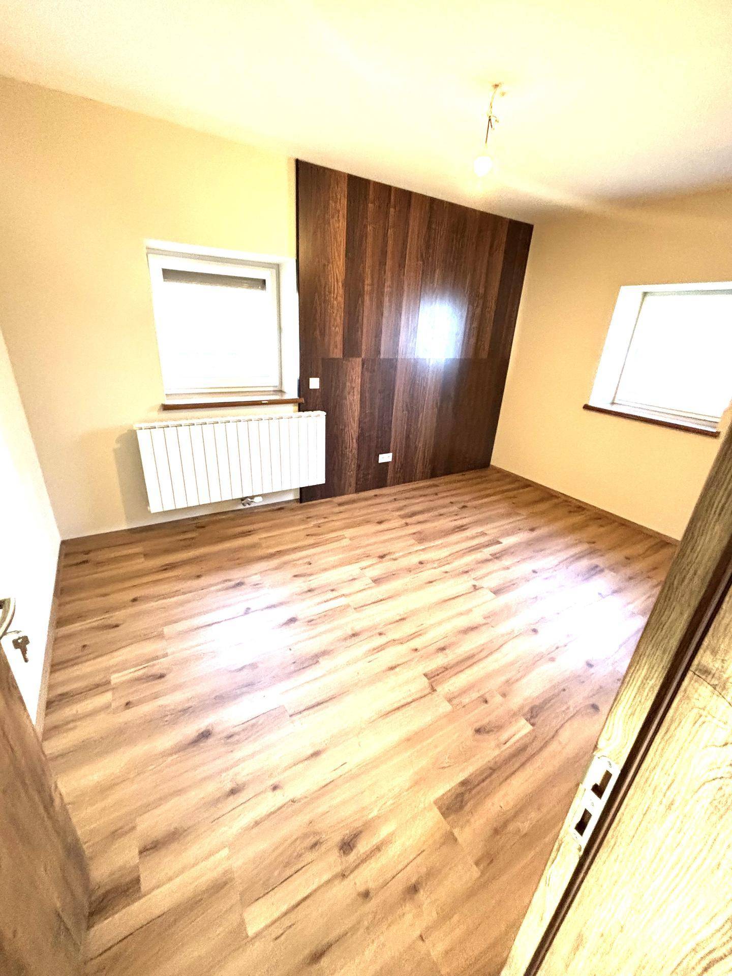 Geräumiges Schlafzimmer mit Laminatboden und einer Holzakzentwand, bietet helle Fenster.