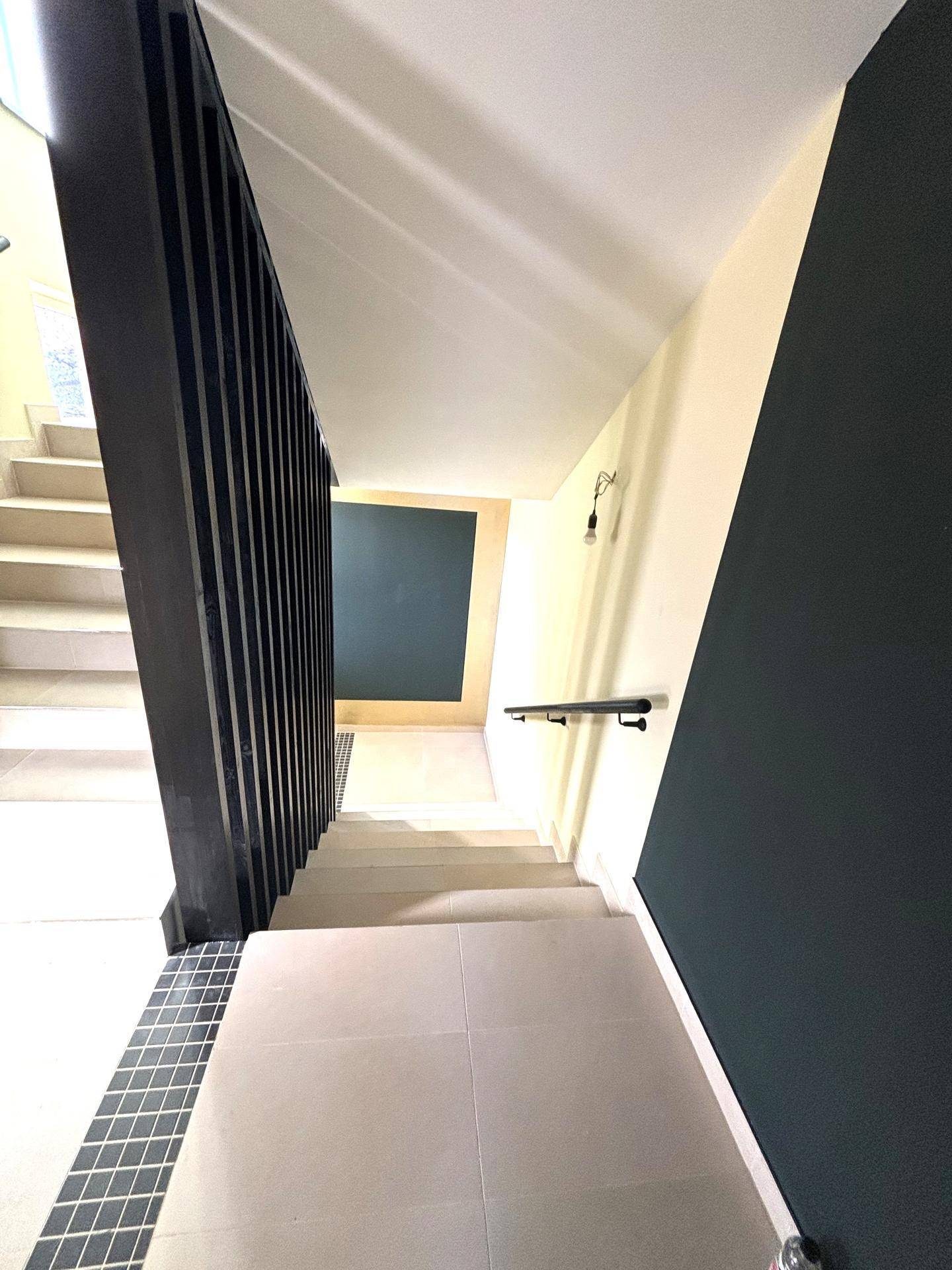 Geräumiges Treppenhaus mit hellen Fliesen und dunklem Geländer, gut beleuchtet durch Tageslicht.