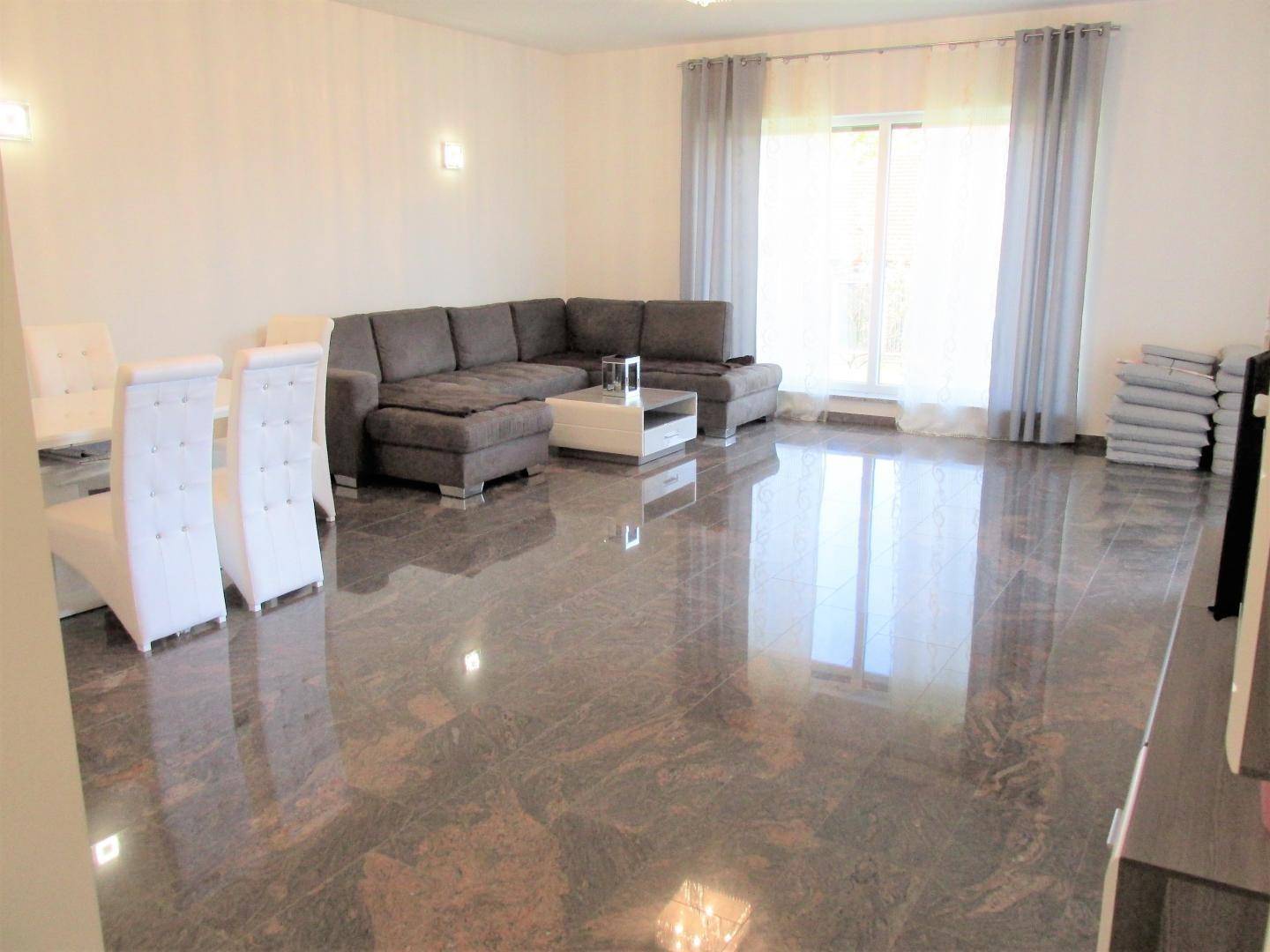 Geräumiger Wohn-Essbereich mit großem Sofa, Esstisch und glänzendem Marmorboden.