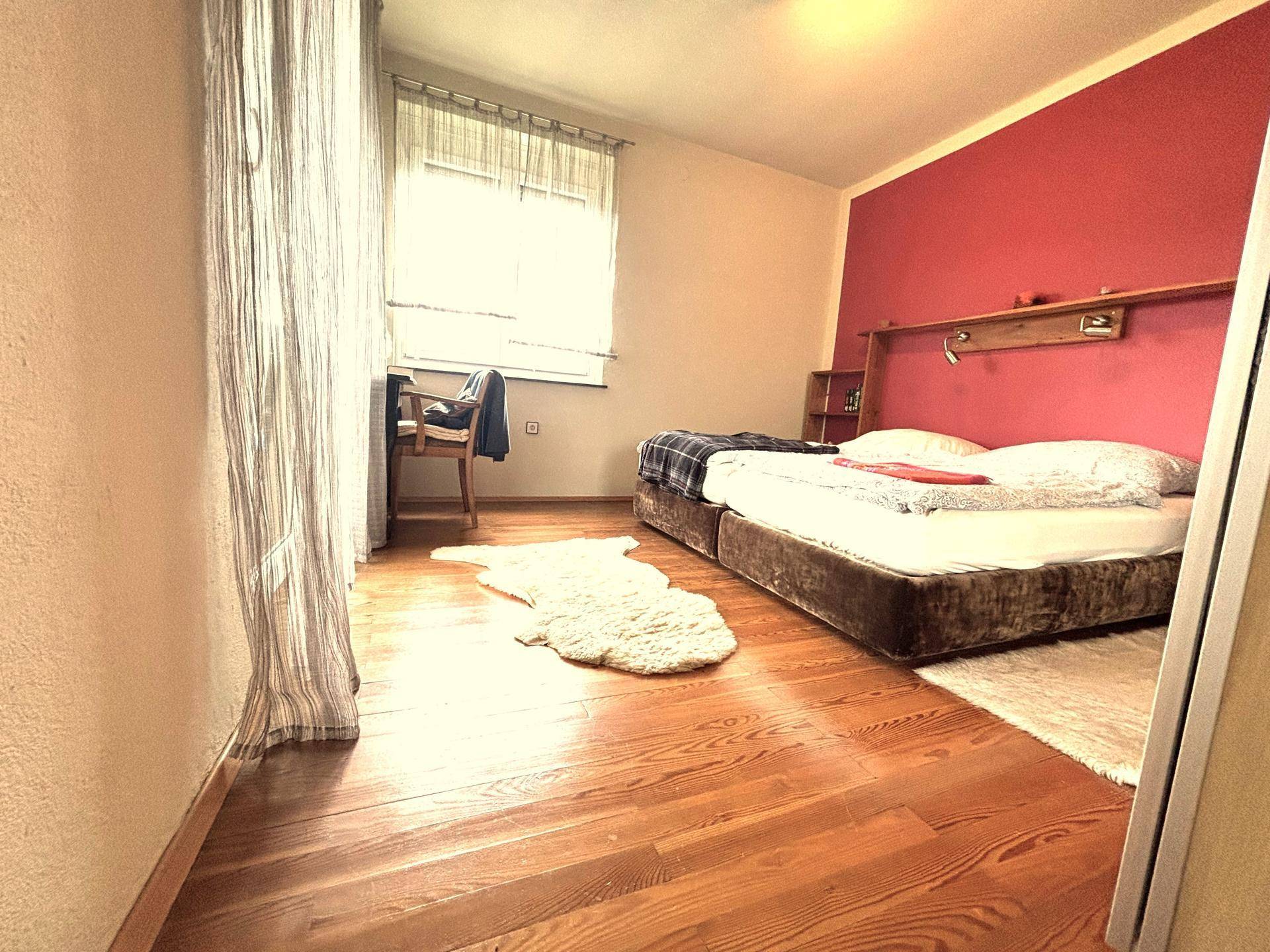 Schlafzimmer mit Holzboden, roter Akzentwand und zwei Einzelbetten.