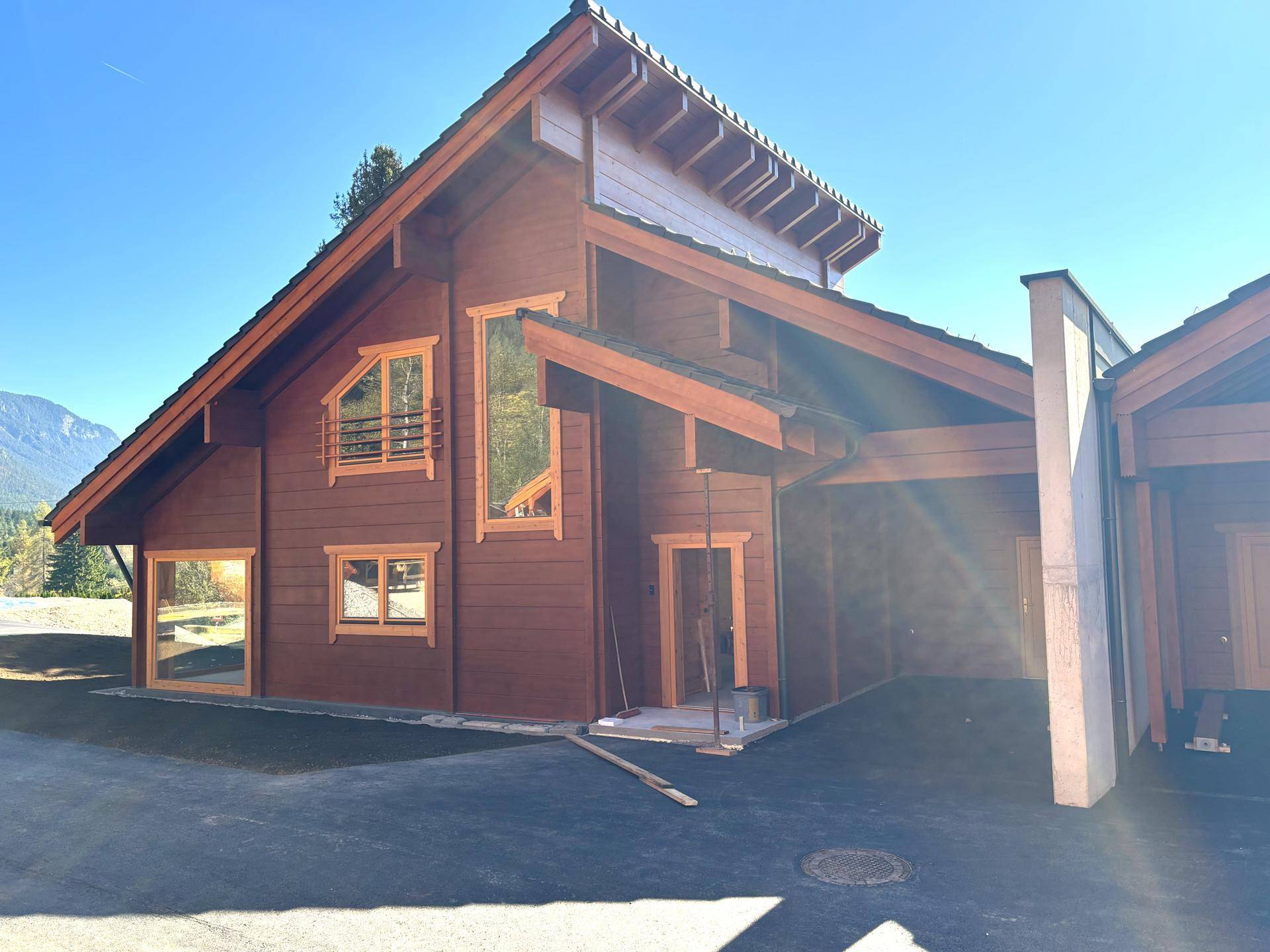 Detailansicht eines neuen Holzhauses mit großen Fenstern, Satteldach und Carport-Bereich.