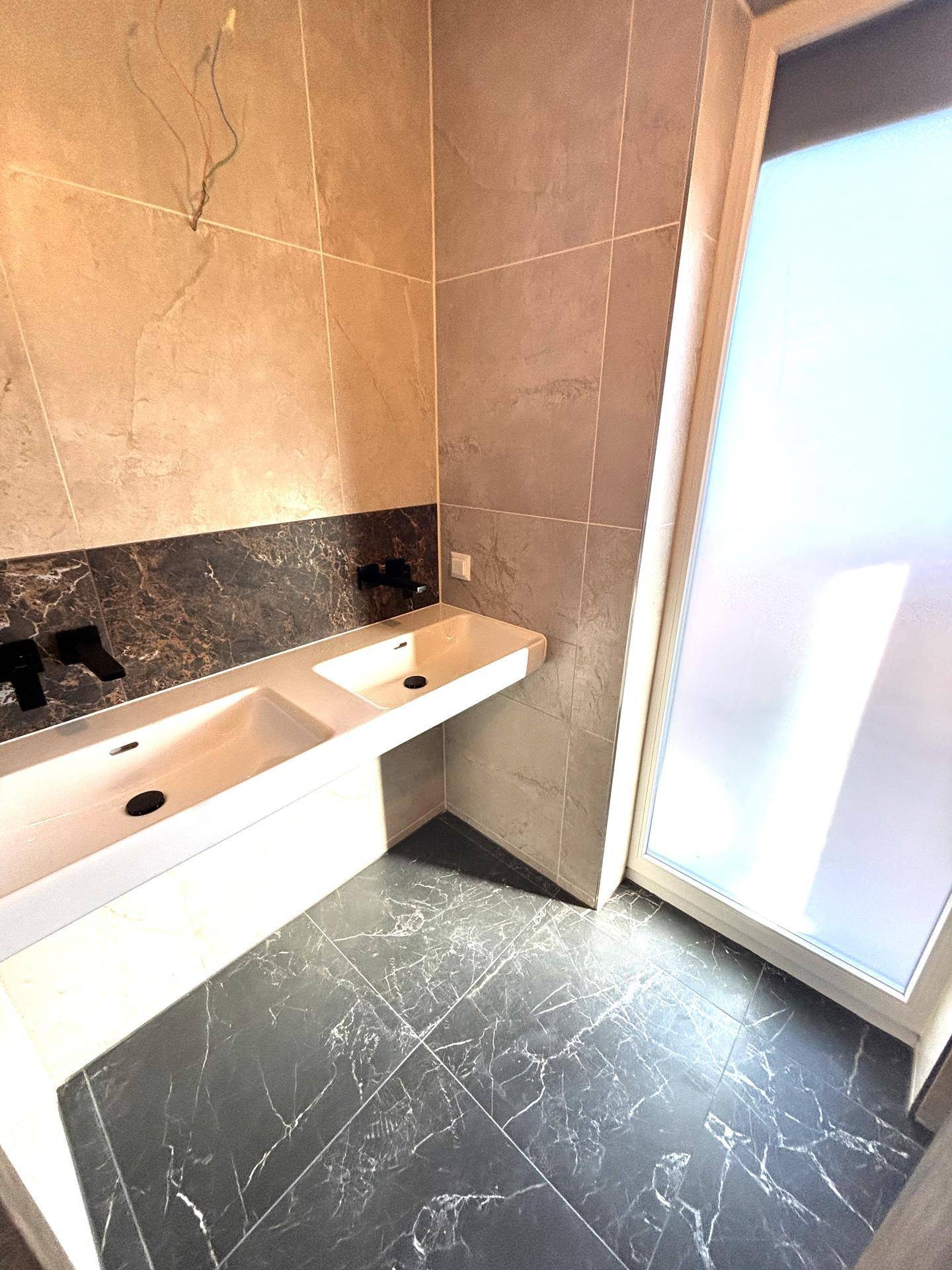 Modernes Badezimmer mit Doppelwaschbecken, dunklen Bodenfliesen und großem Fenster.
