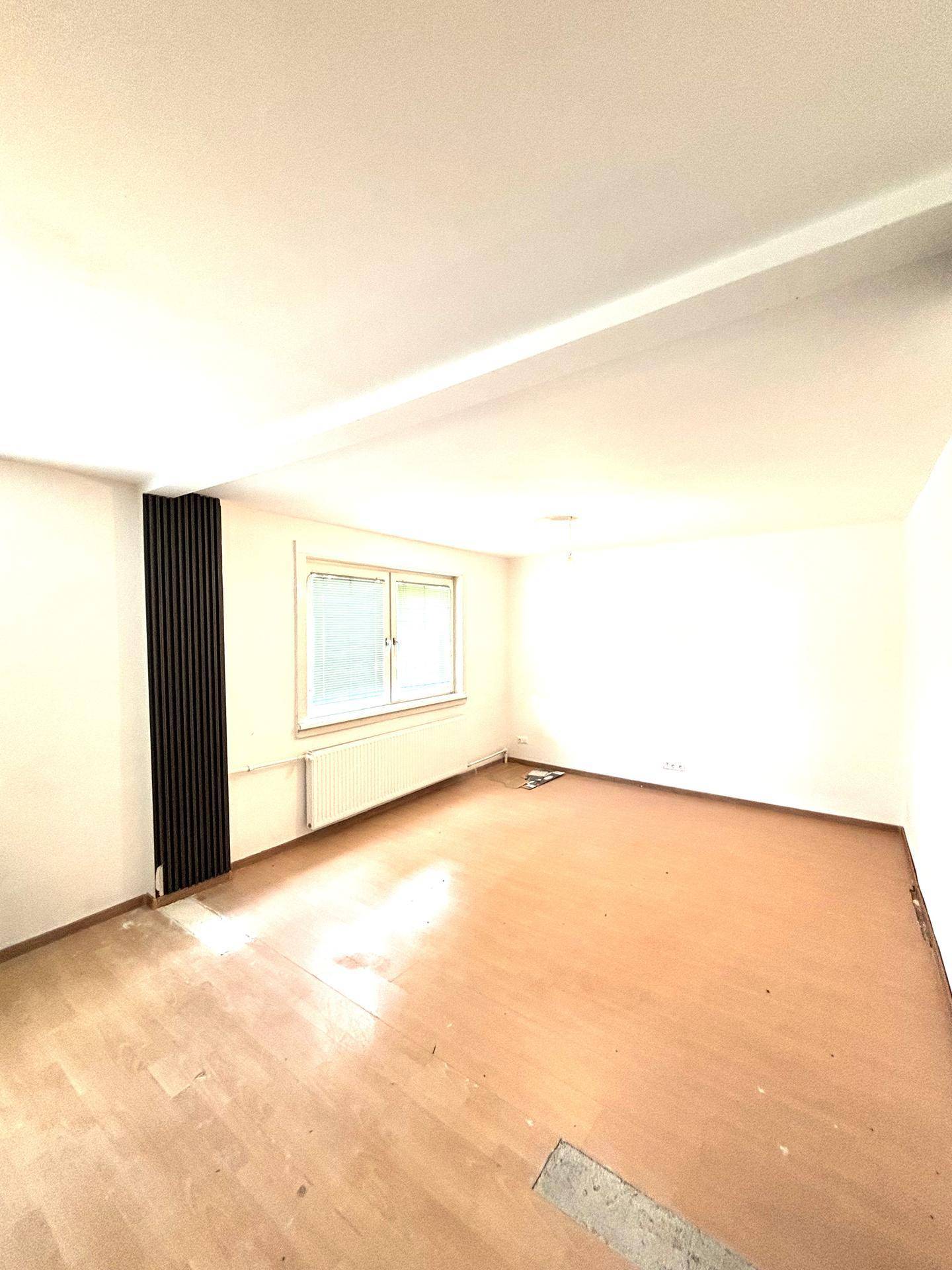 Leeres Wohnzimmer mit hellem Laminatboden und einem Fenster, bereit zur Gestaltung.
