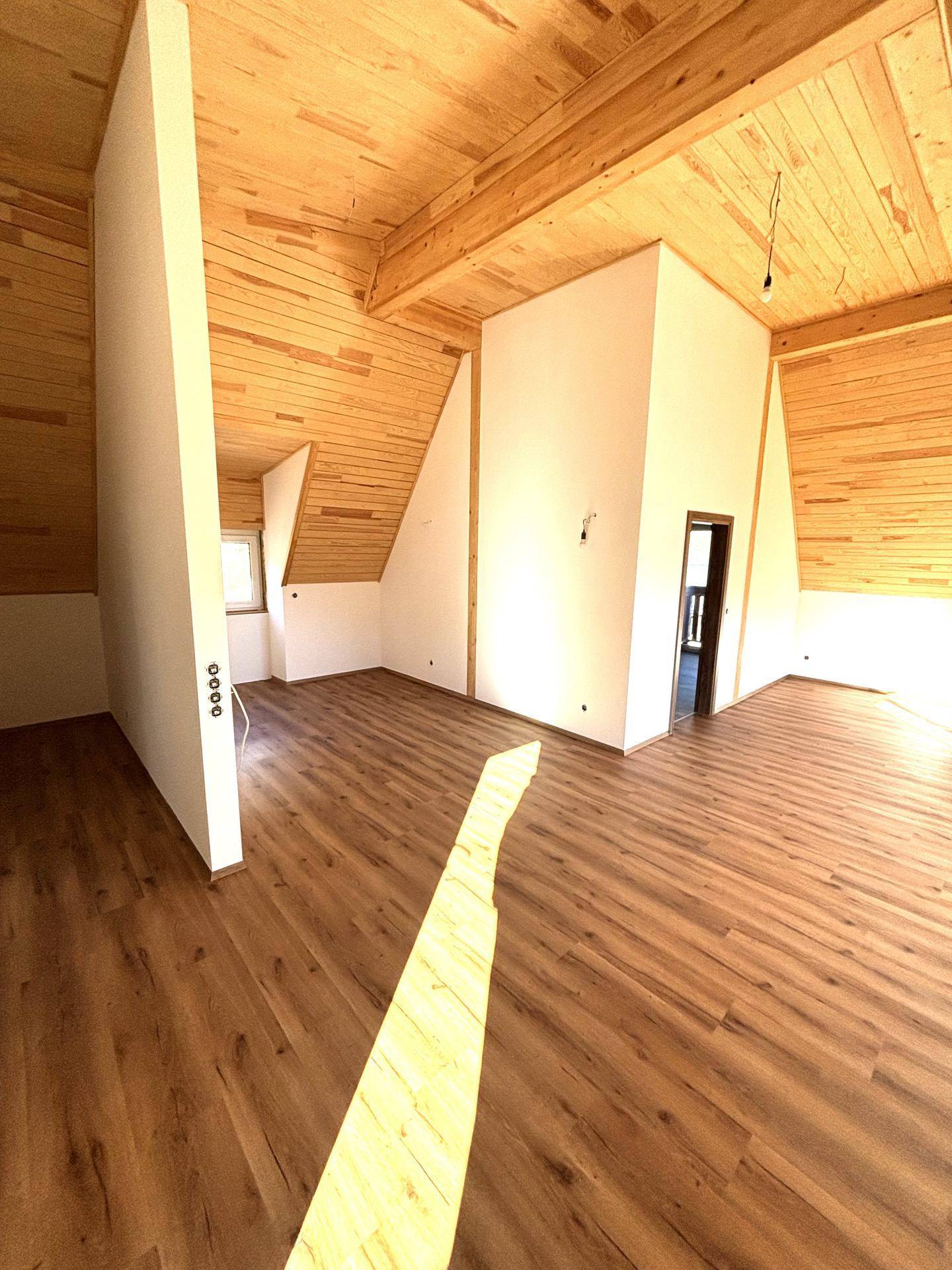 Offener Wohnbereich mit hohen Holzdecken und Laminatboden, bereit für die Einrichtung.