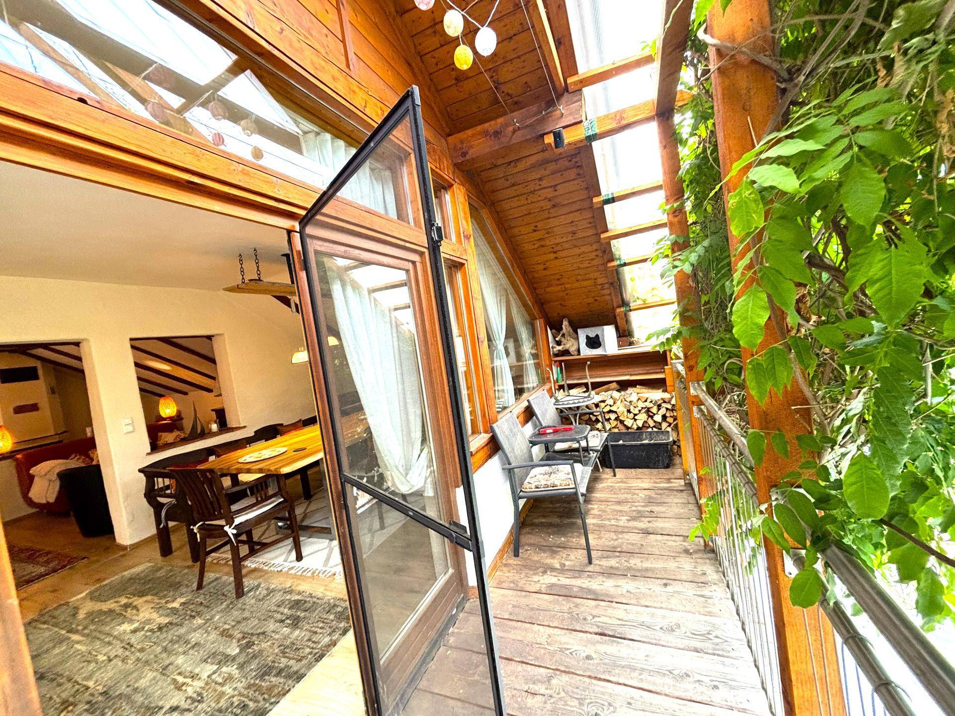 Überdachter Balkon mit Sitzgelegenheiten, Holzverkleidung und Blick ins Grüne.