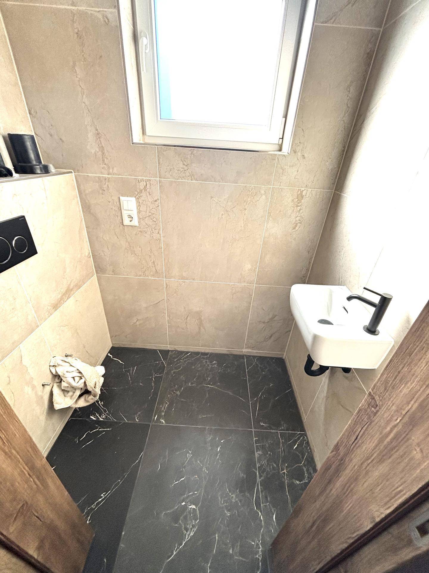 Modernes Gäste-WC mit dunklen Bodenfliesen, beigen Wandfliesen und einem kleinen Waschbecken.
