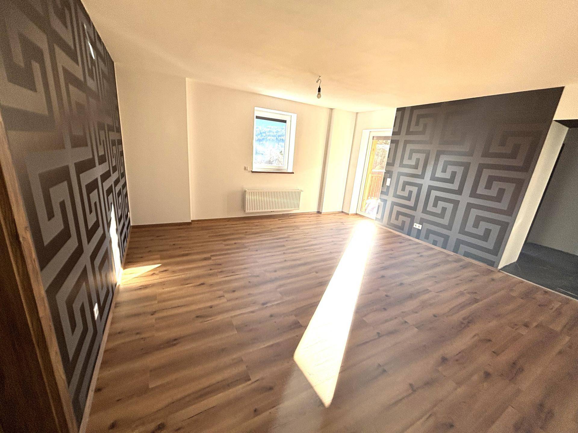 Geräumiger Wohnbereich mit Laminatboden und zwei Akzentwänden mit geometrischem Muster.
