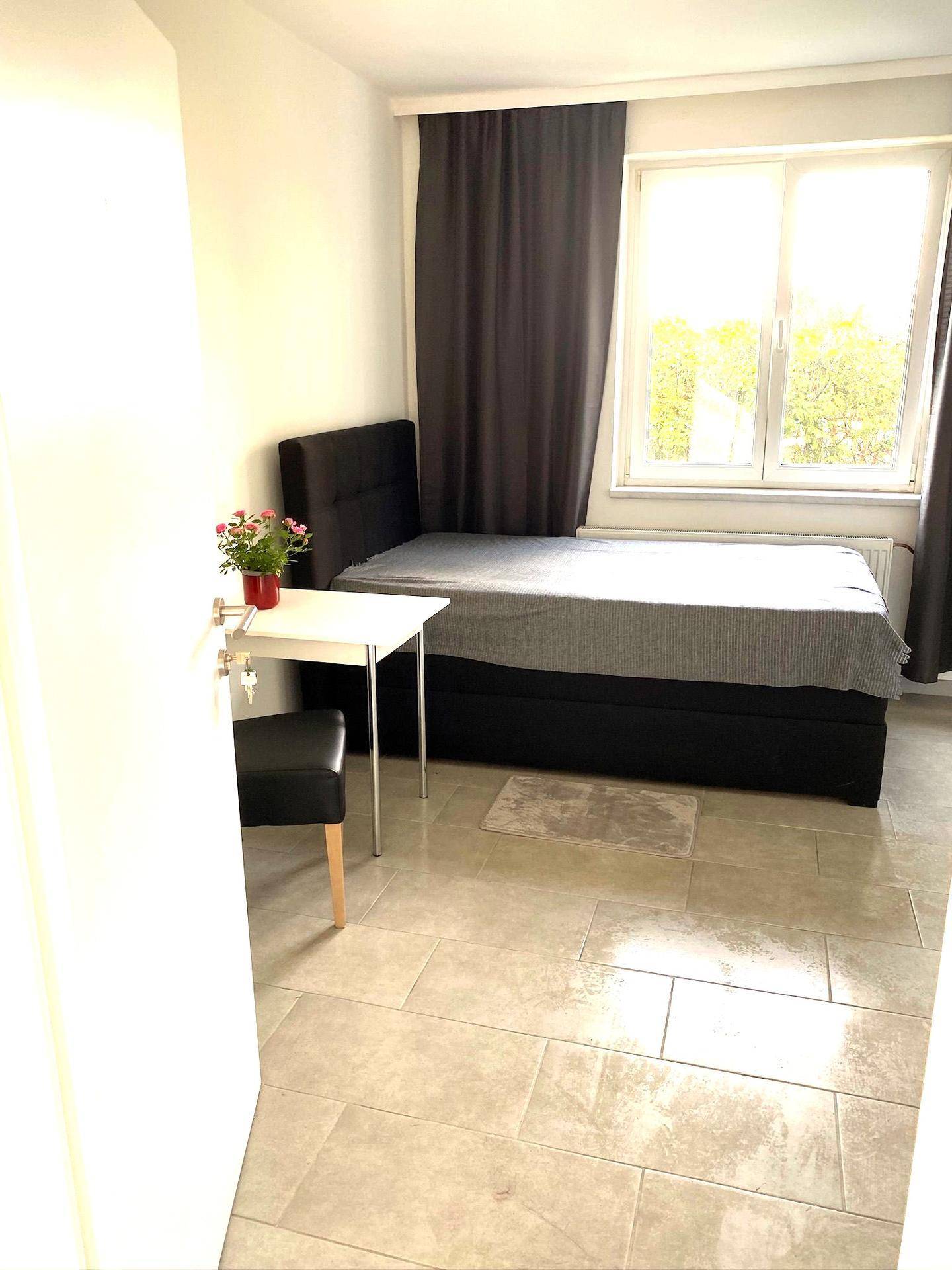Helles Schlafzimmer mit Fliesenboden, Doppelbett und großem Fenster.