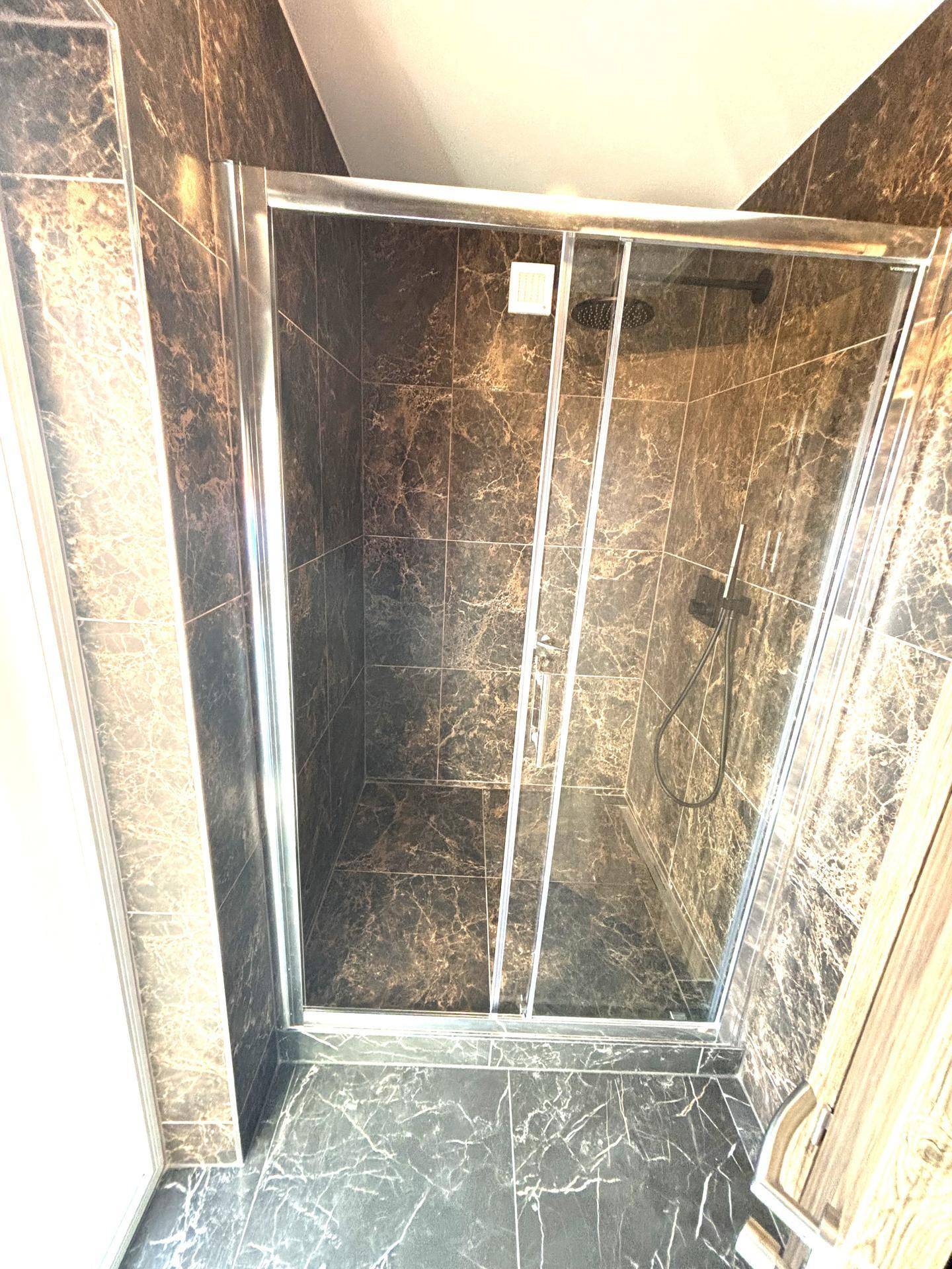 Moderne Duschkabine mit dunklen Marmorfliesen und Glasabtrennung im Badezimmer.