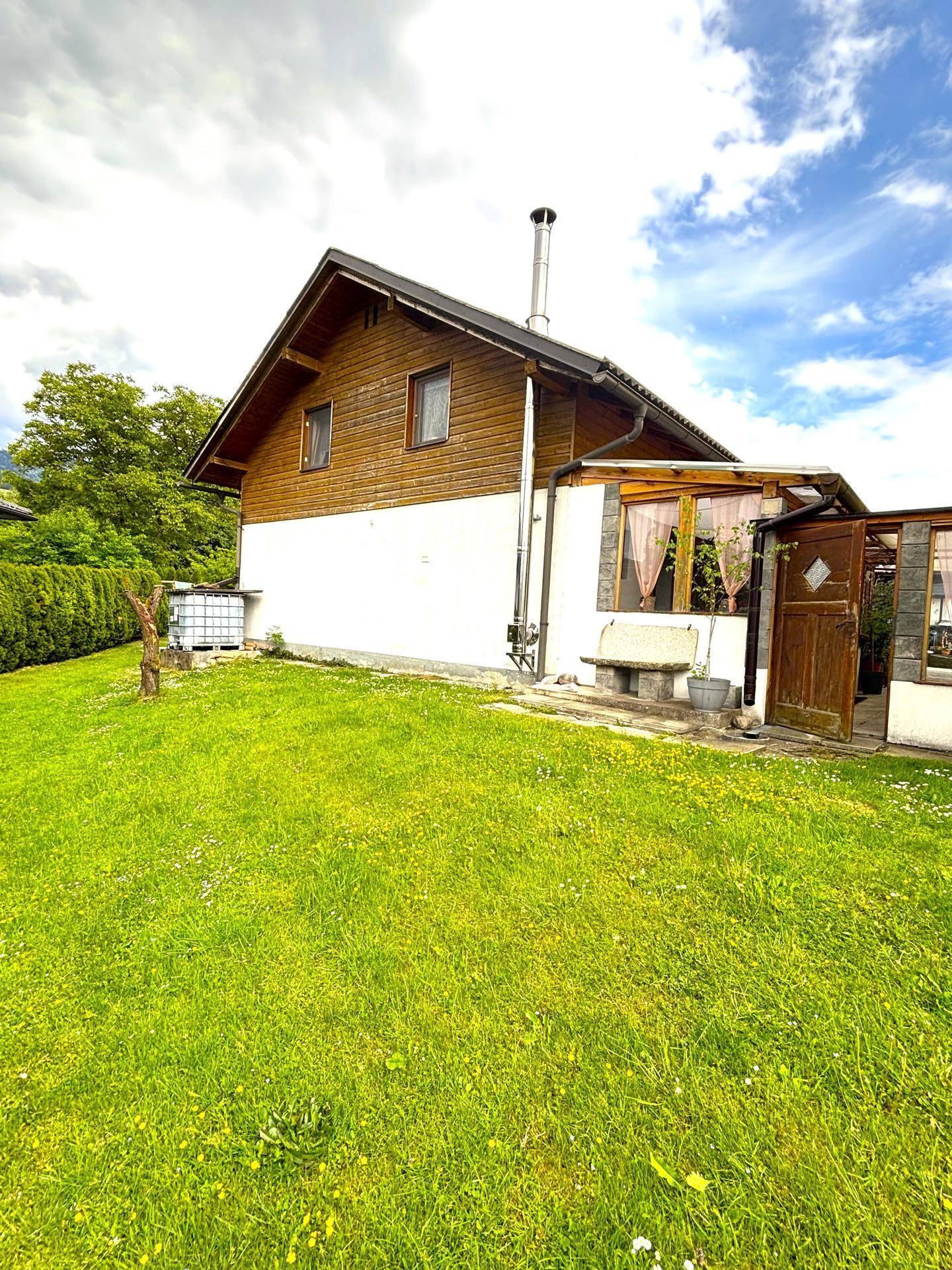 Charmantes Holzhaus mit weißer Fassade und grünem Garten unter bewölktem Himmel.