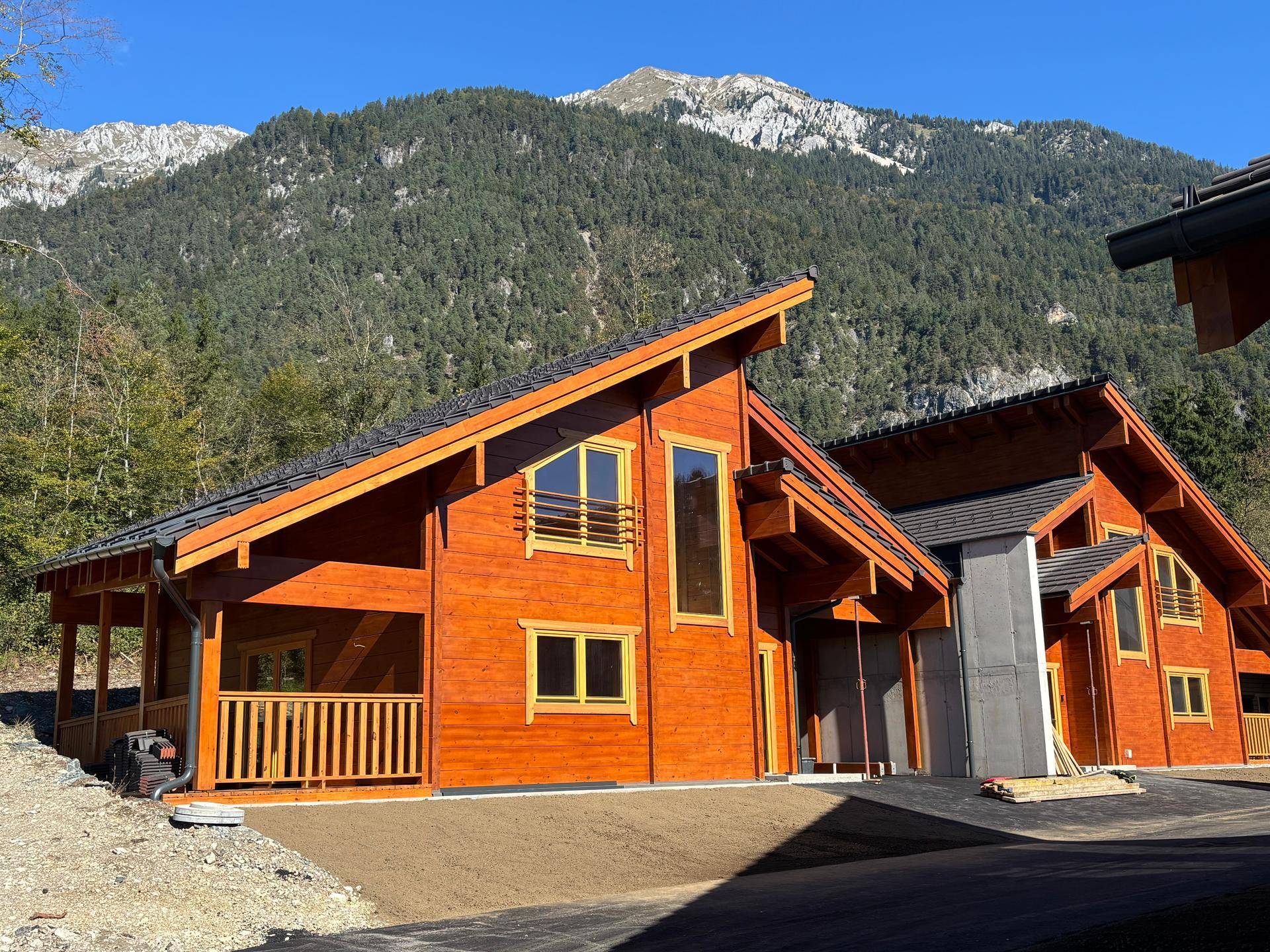 Zwei neu gebaute Holzhäuser mit traditionellen Dächern und Bergblick in einer idyllischen alpinen Umgebung.
