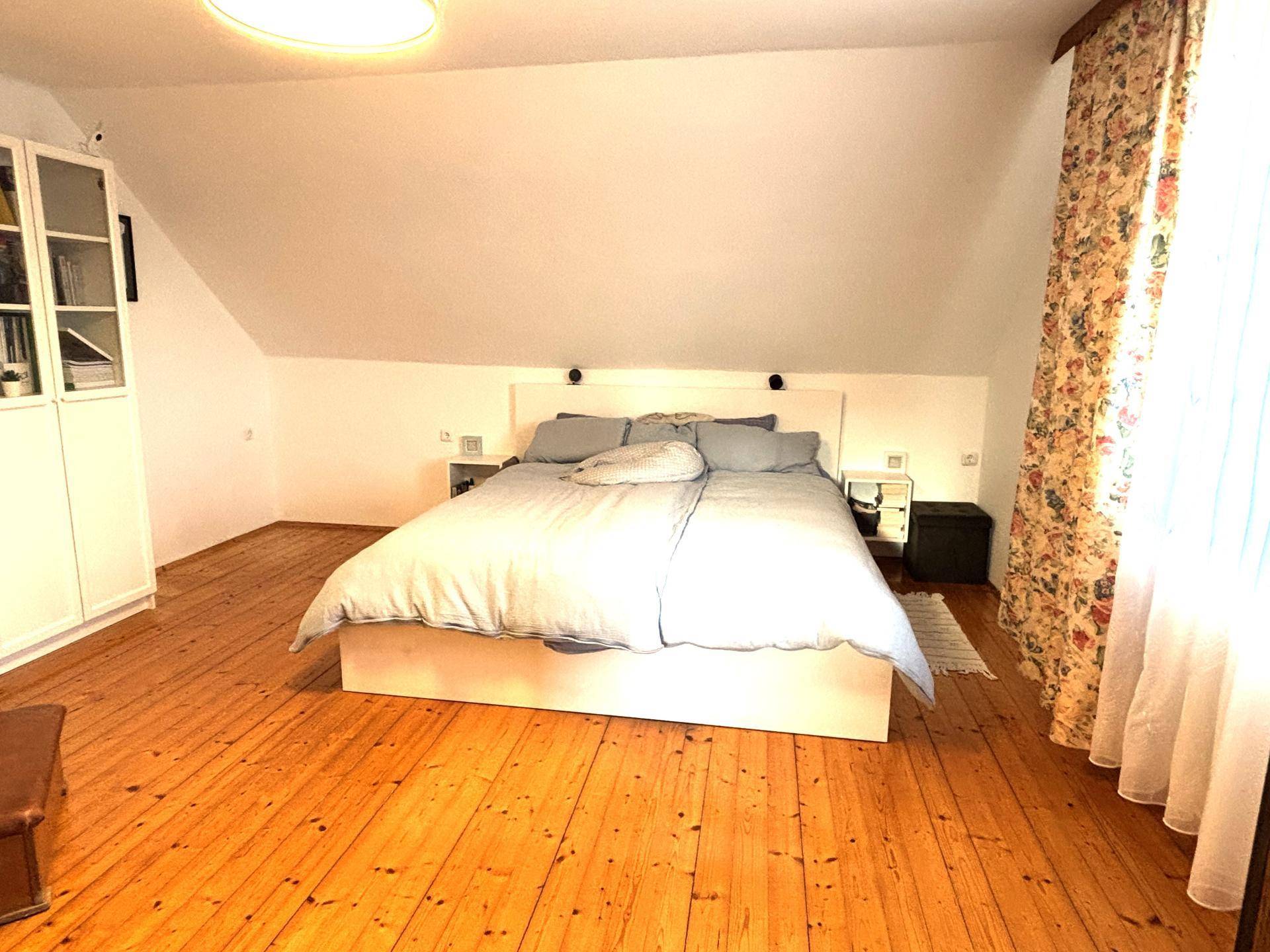 Helles Schlafzimmer im Dachgeschoss mit Holzdielenboden, Dachschräge und einem großen Doppelbett.