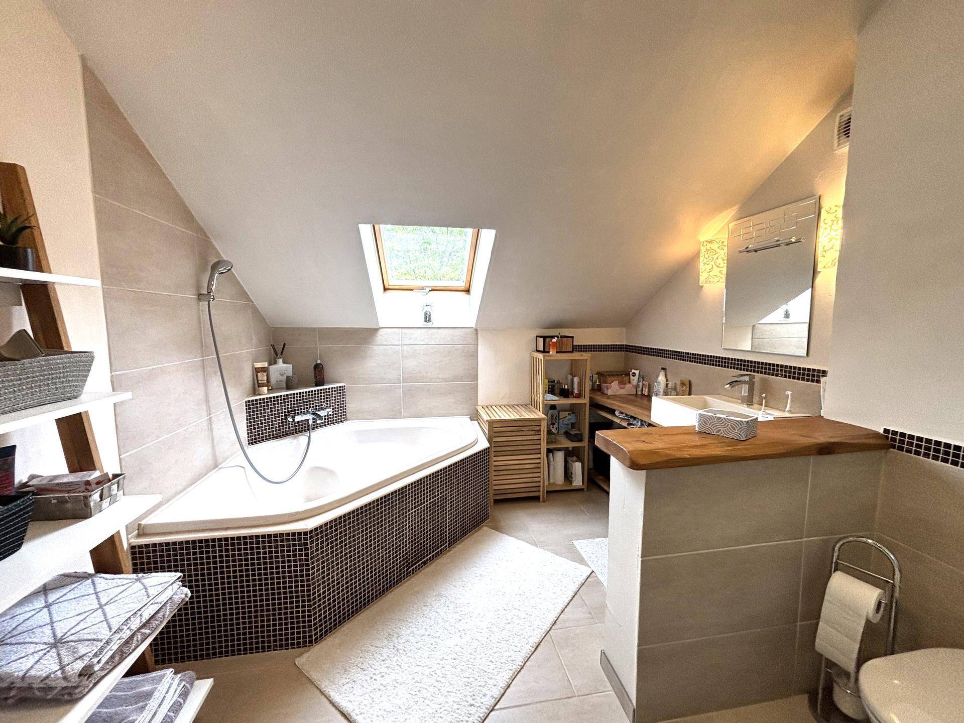 Modernes Badezimmer im Dachgeschoss mit Eckbadewanne, Dachfenster und hellen Fliesen.