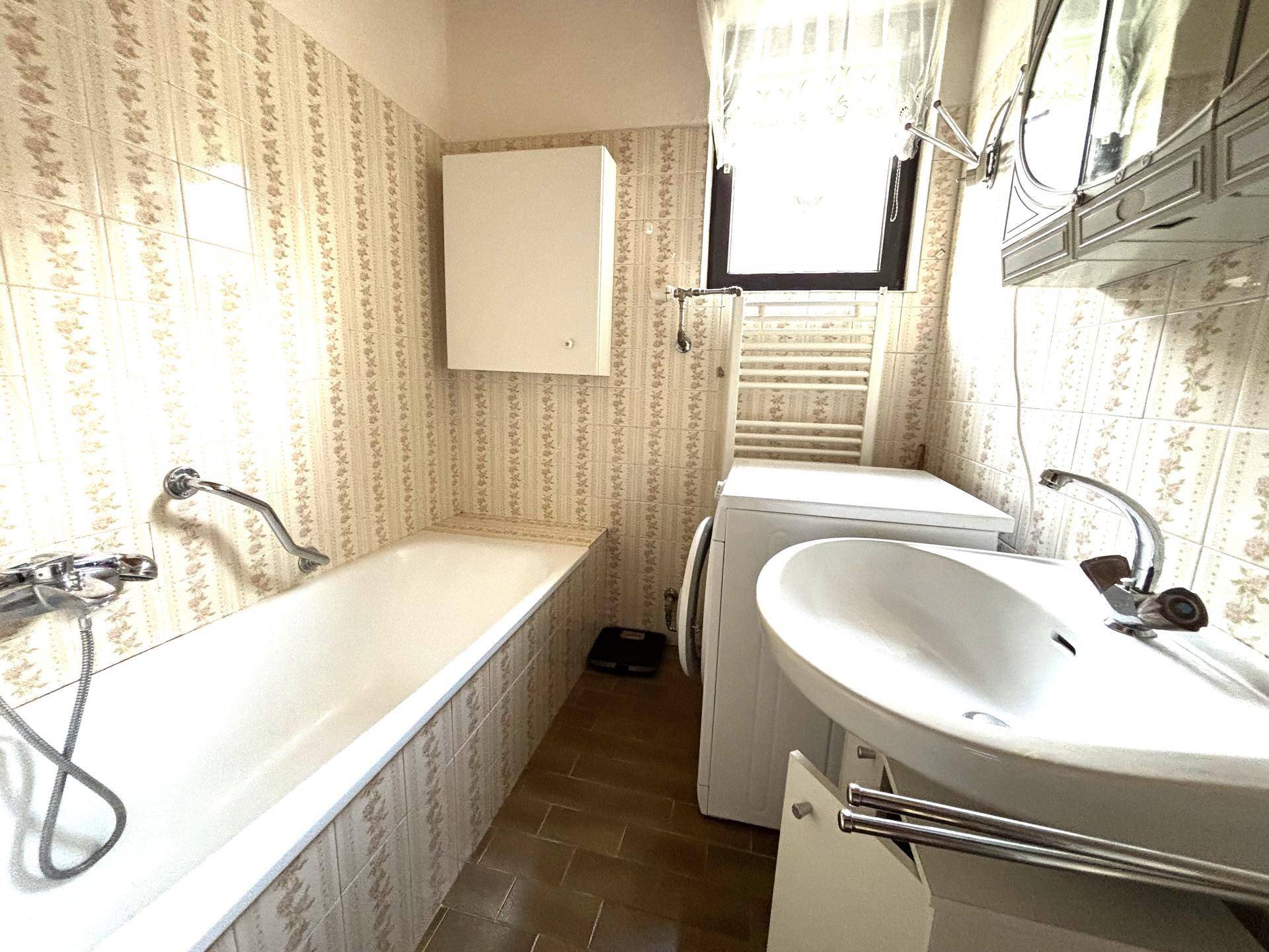 Badezimmer mit Badewanne, Waschmaschine und Fenster.