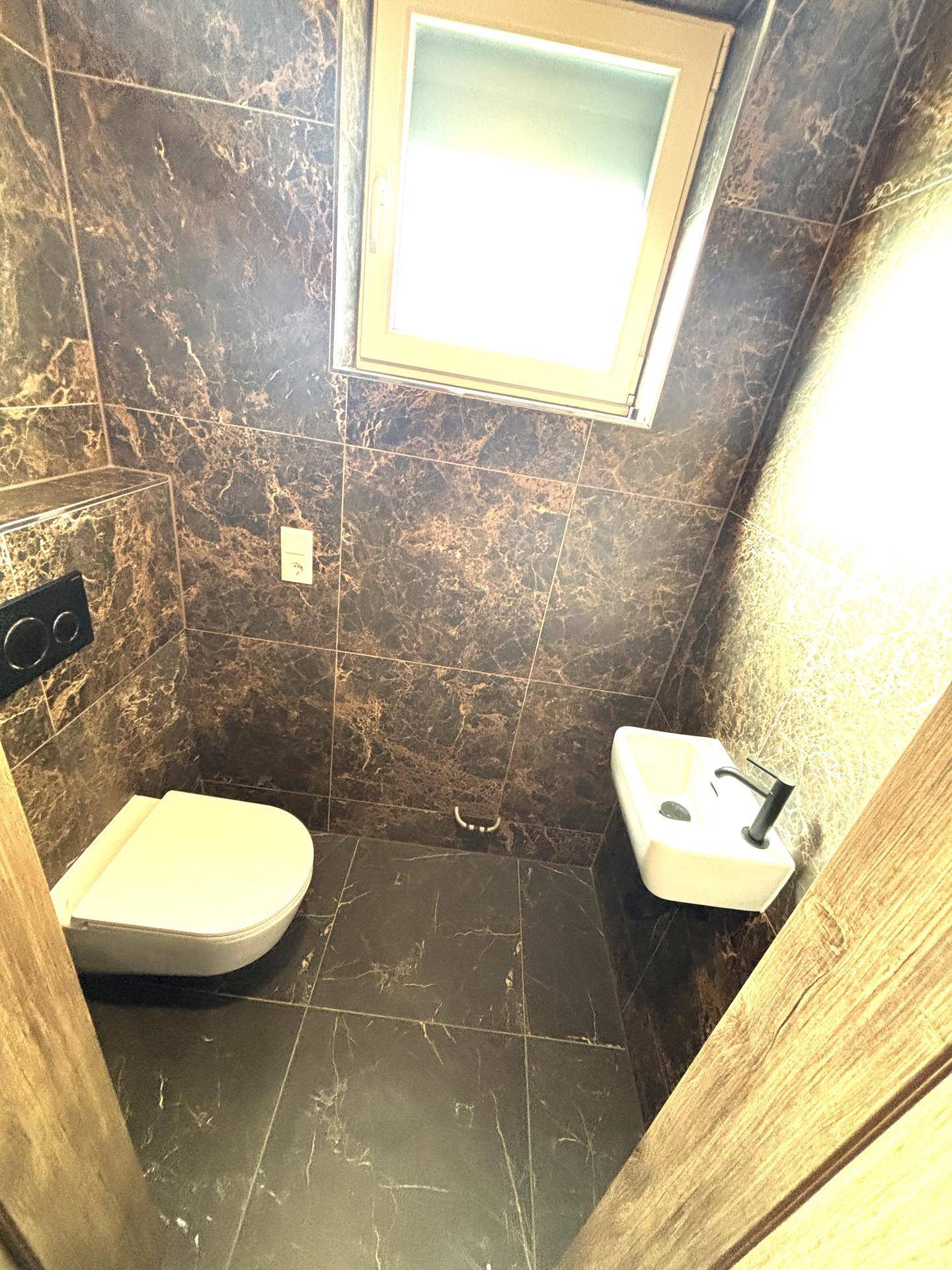 Modernes Gäste-WC mit dunklen Marmorfliesen, wandhängendem WC und kleinem Waschbecken.