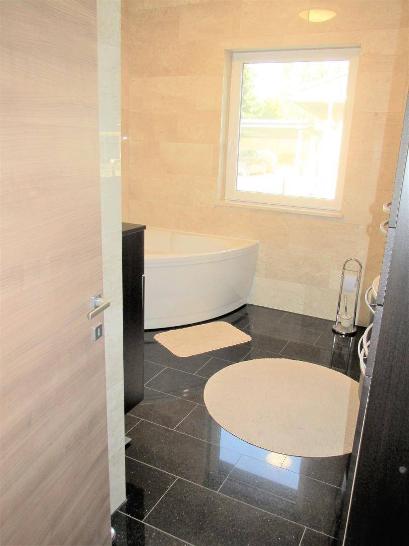 Badezimmer mit dunklem Fliesenboden, Eckbadewanne und Fenster für Tageslicht.