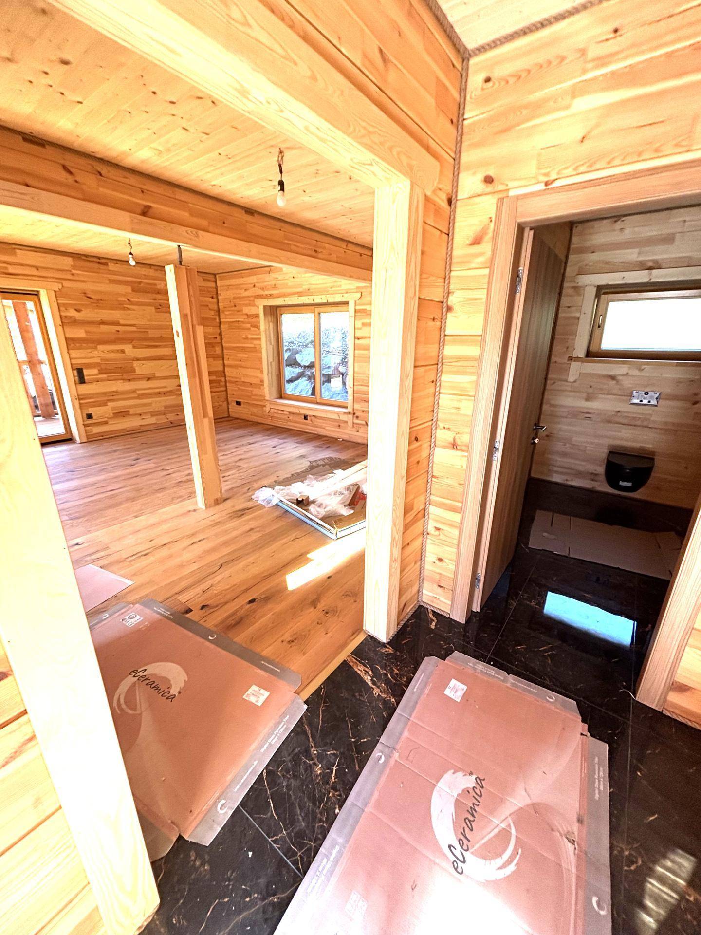 Lichtdurchfluteter Innenraum in Holzbauweise mit Holzboden und Blick in einen weiteren, offenen Raum.