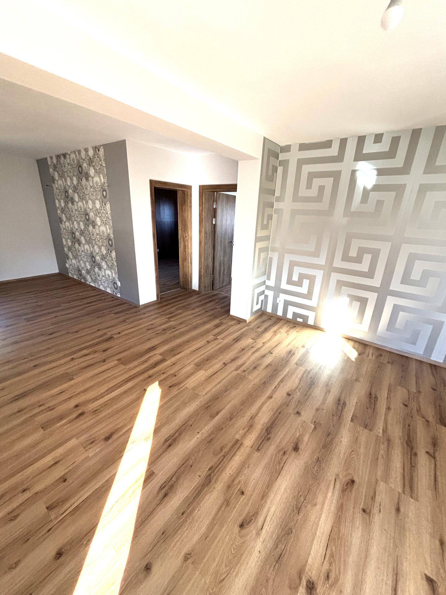 Helles Wohnzimmer mit Laminatboden und einer modernen geometrischen Tapete an der Wand.