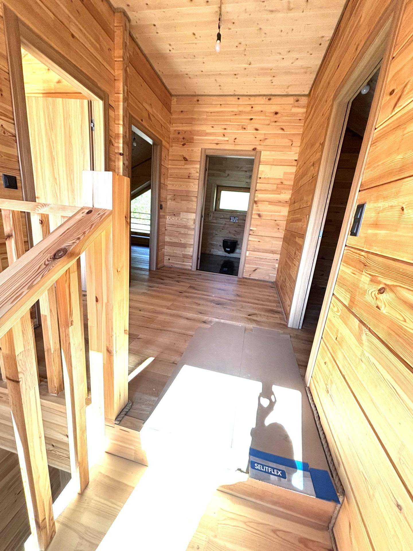 Heller Flur mit Holztreppe und Blick in ein modernes Badezimmer mit dunklen Fliesen.