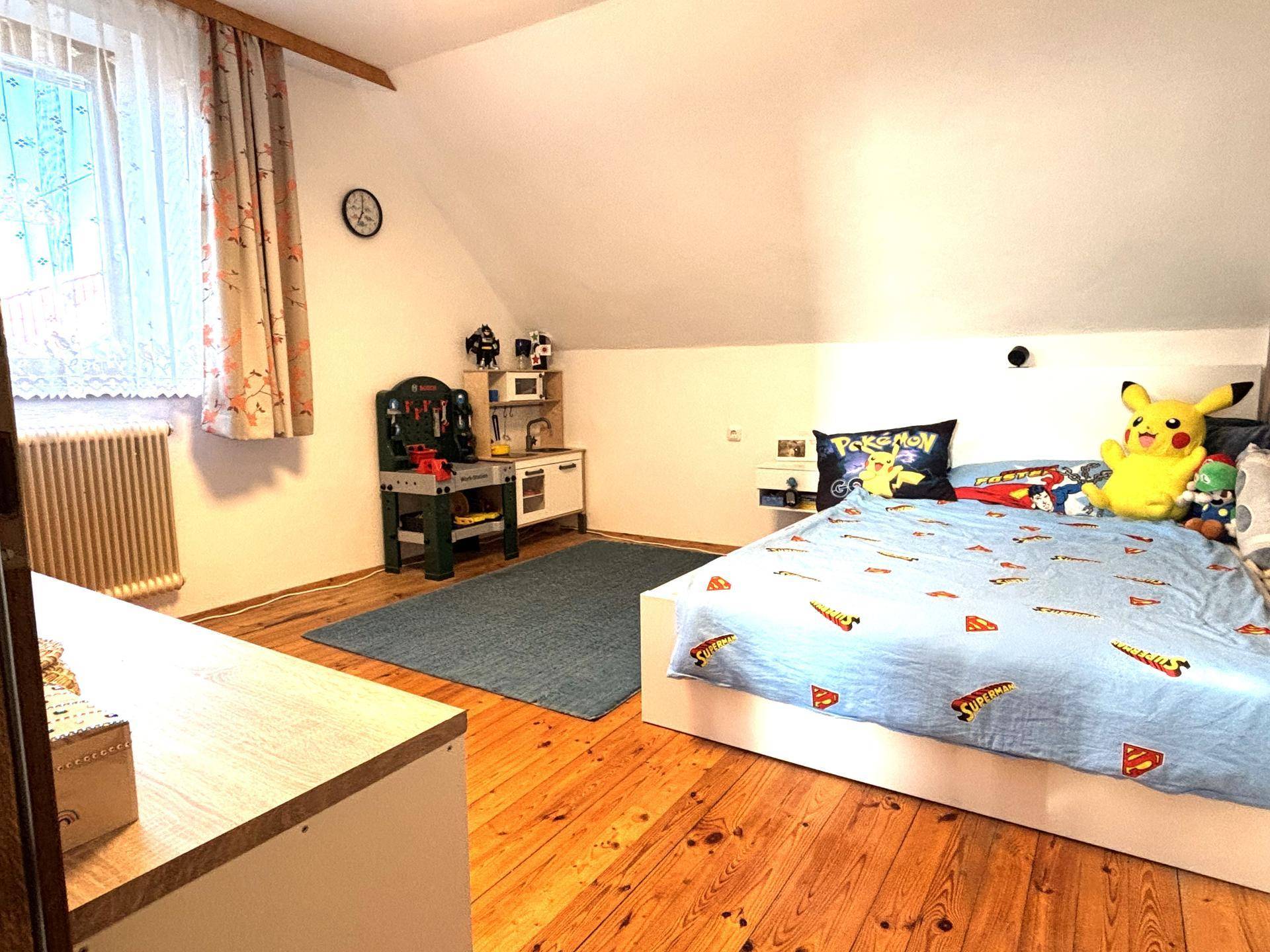 Kinderzimmer im Dachgeschoss mit Holzdielenboden, Dachschräge und einem Einzelbett mit Spielzeug.