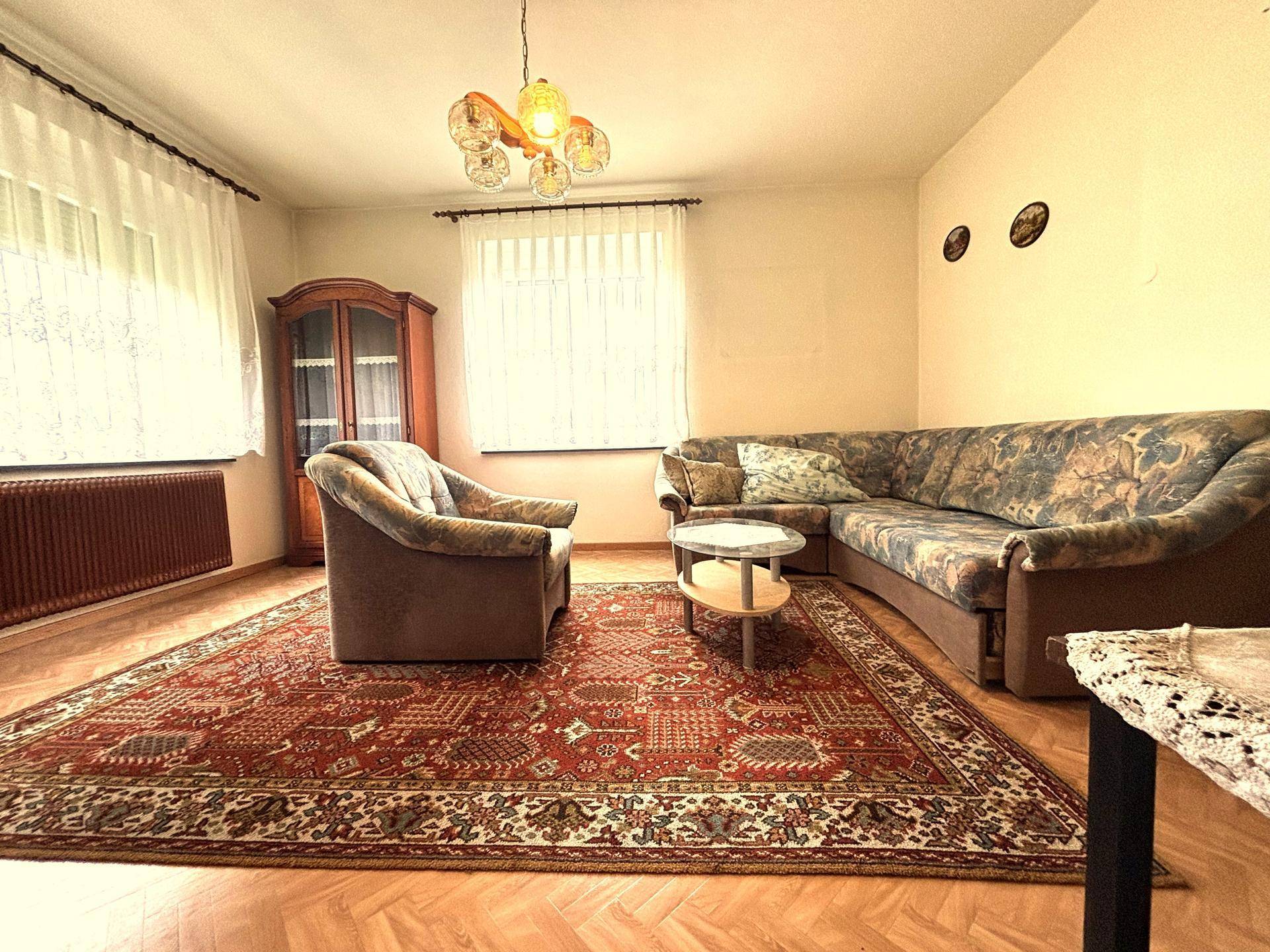 Geräumiges Wohnzimmer mit traditionellem Teppich, Ecksofa und Holzschrank.