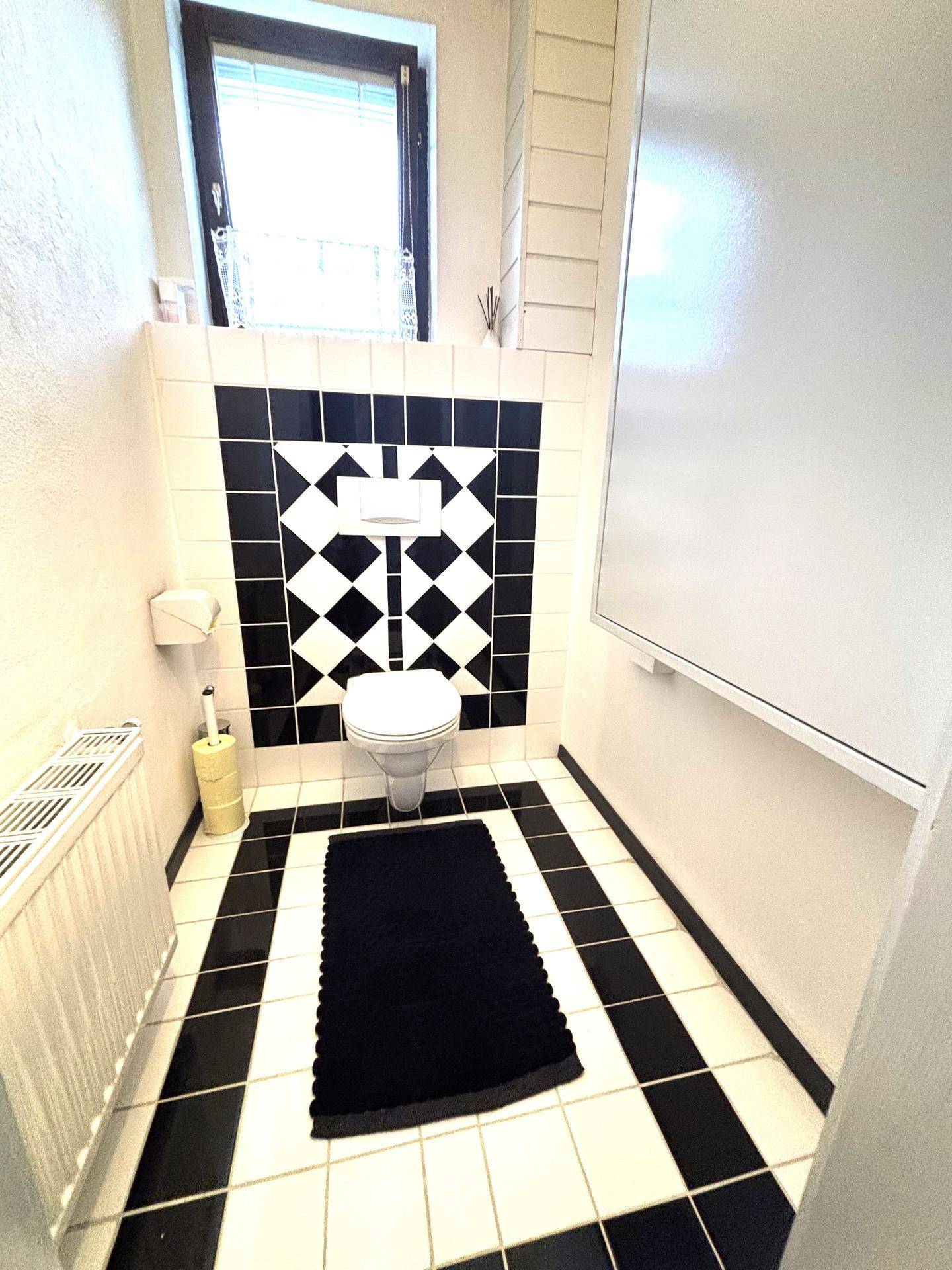 Separate Toilette mit schwarz-weißen Fliesen und Fenster.