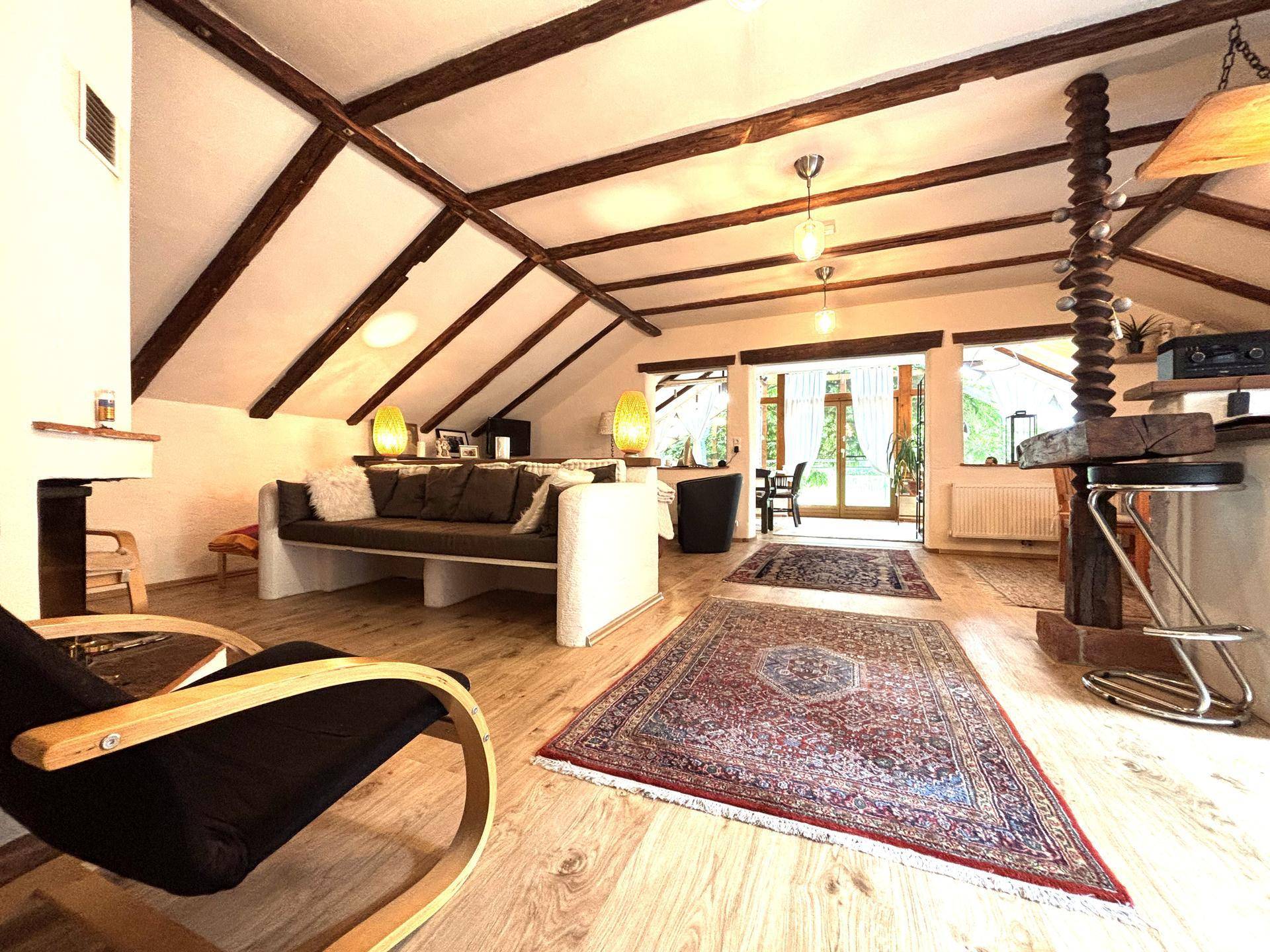 Geräumiges Wohnzimmer im Dachgeschoss mit Holzbalken, Parkettboden und Zugang zum Wintergarten.