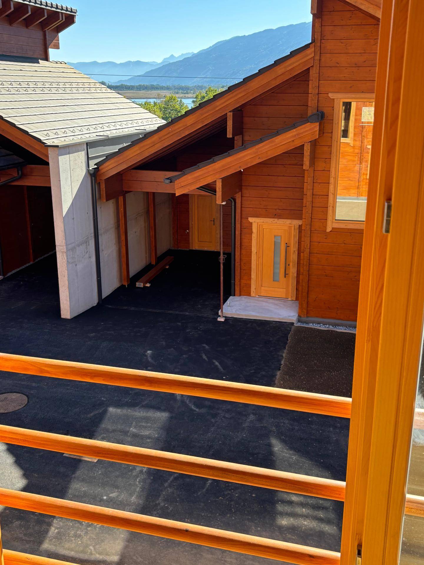 Blick von einem Fenster auf den Eingangsbereich des Holzhauses und die umliegende Landschaft.