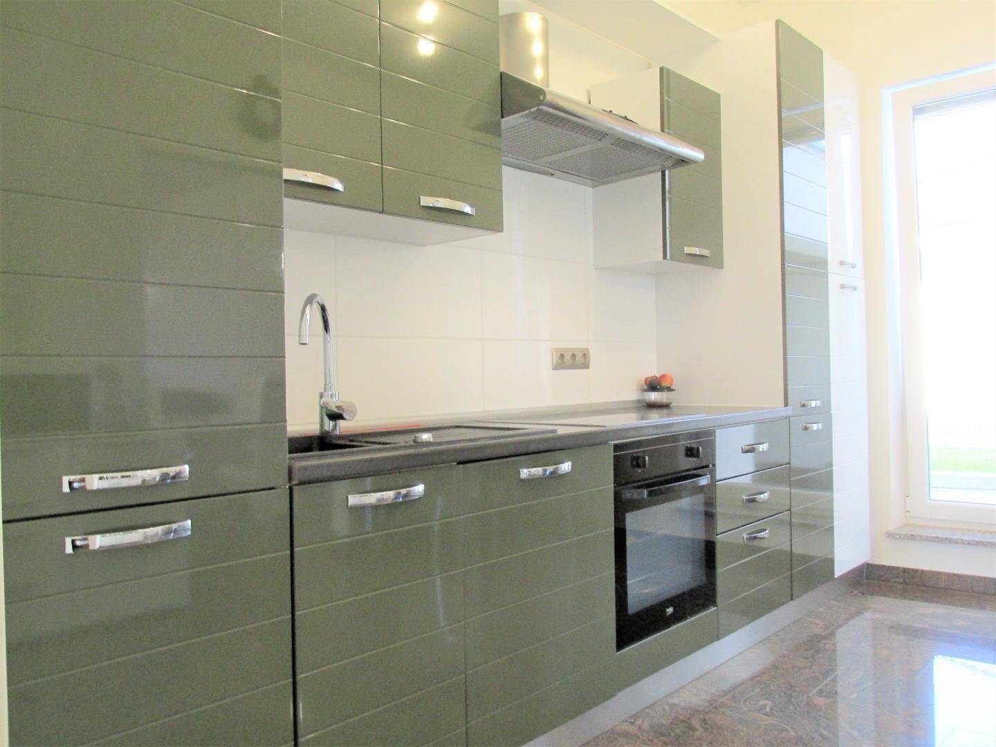 Moderne Küche mit glänzenden grünen Fronten, Einbaugeräten und Fenster.