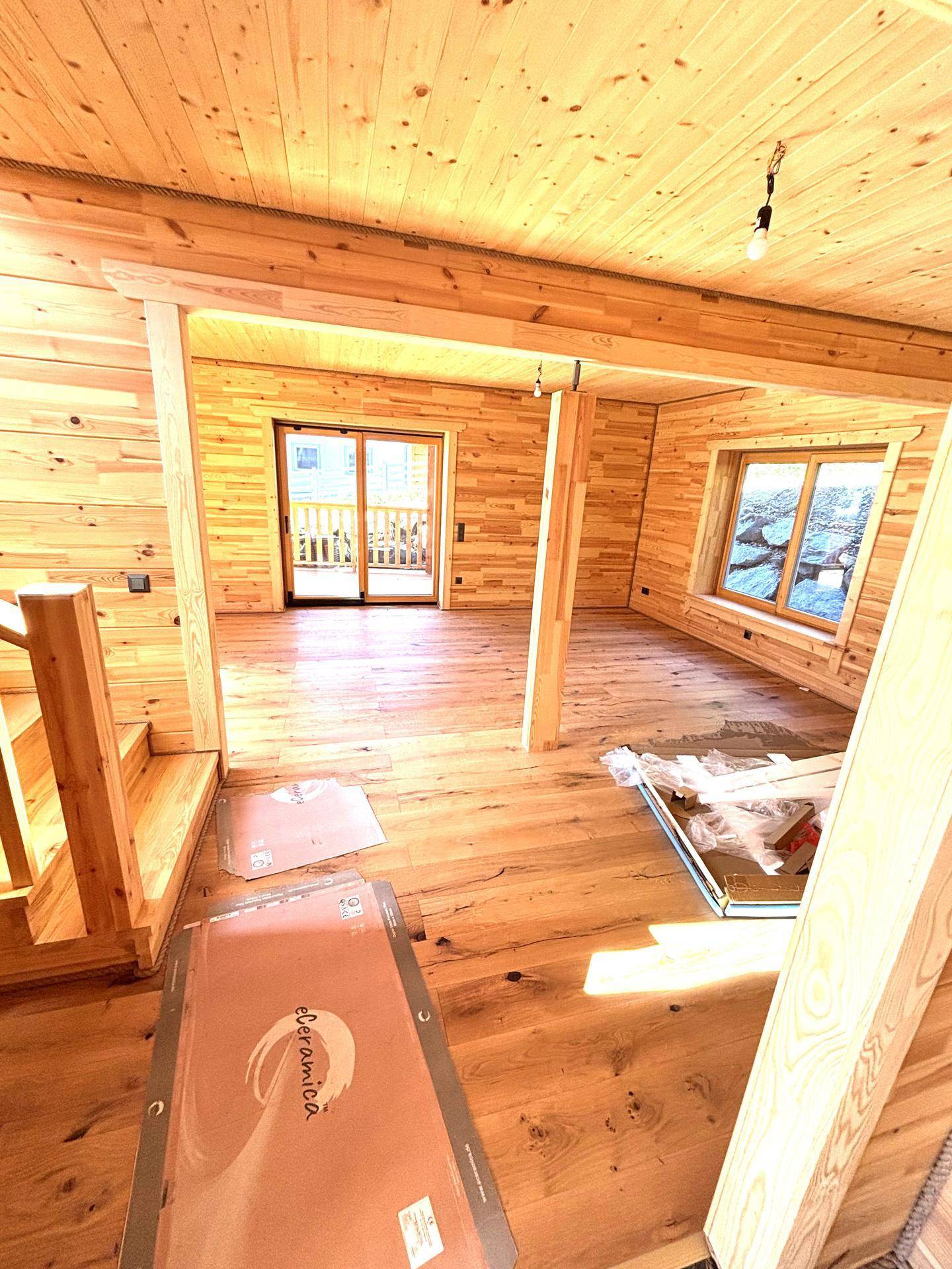 Geräumiges Wohnzimmer mit Holzvertäfelung, Holzboden und Zugang zu einem Balkon.